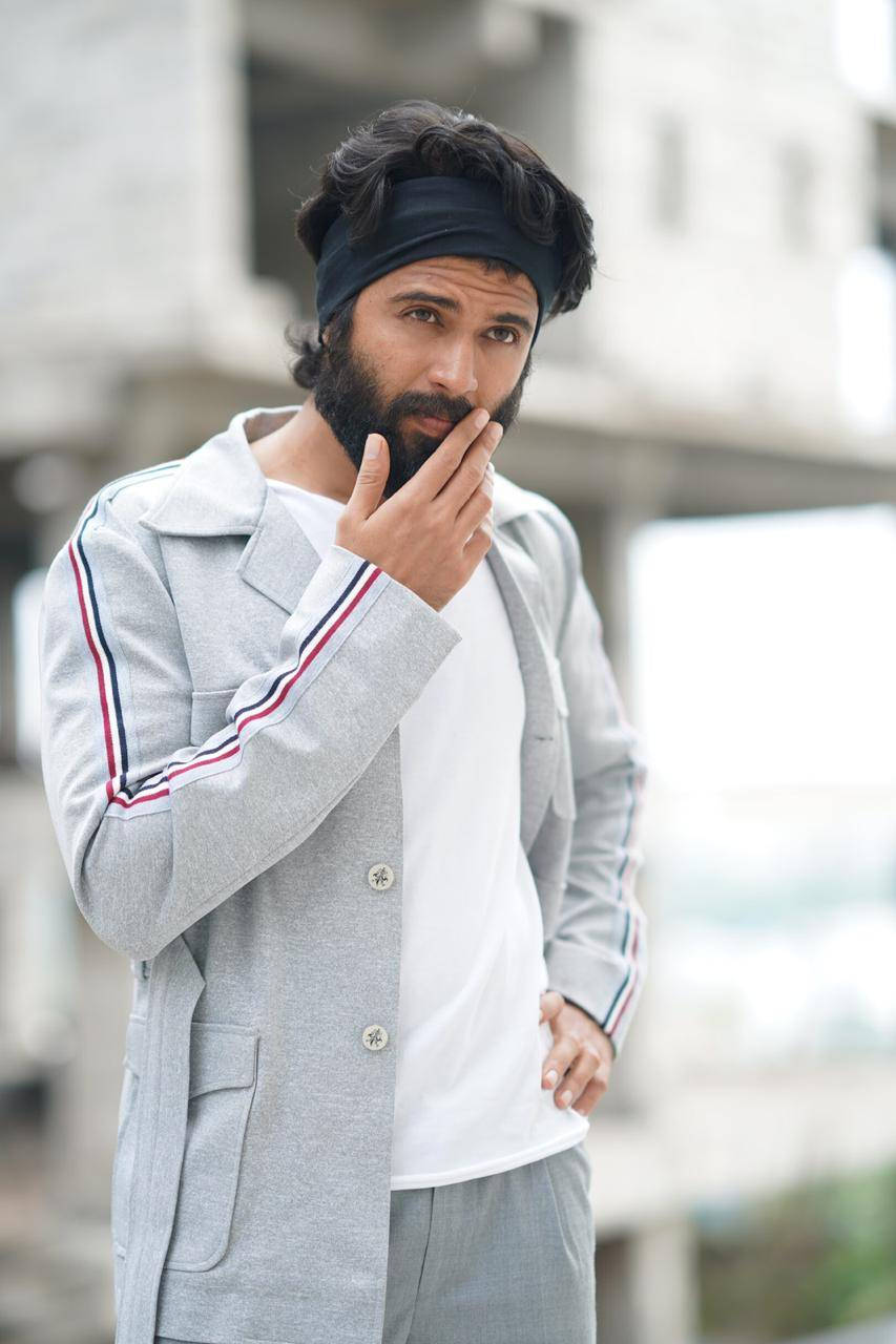 Indian 桌布 壁紙 — 一位留鬍鬚的男子穿著灰色運動外套和頭帶，在模糊的城市背景下，手靠近下巴若有所思地擺姿勢。