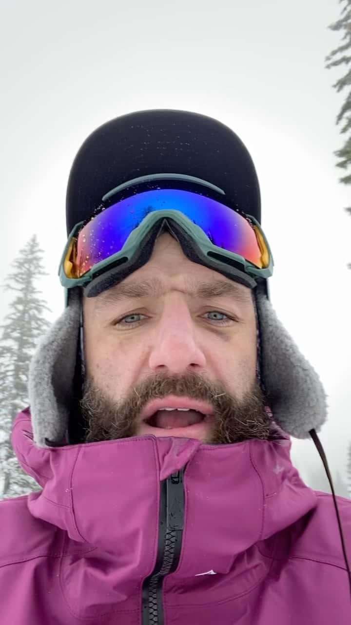 MMA 桌布 壁紙 — 一位留鬍鬚的男子穿著紫色滑雪外套和護目鏡，站在雪地森林中，身後有松樹。