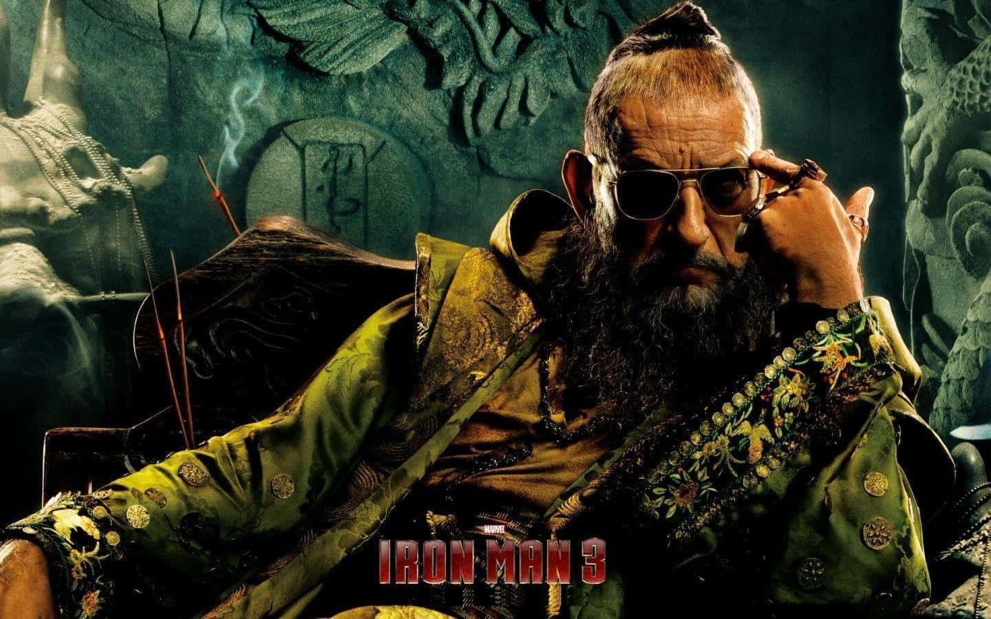 Villain 桌布 壁紙 — 一位留鬍鬚的男子身穿華麗的綠色長袍，坐在一個有雕刻石牆的寺廟環境中吸煙。