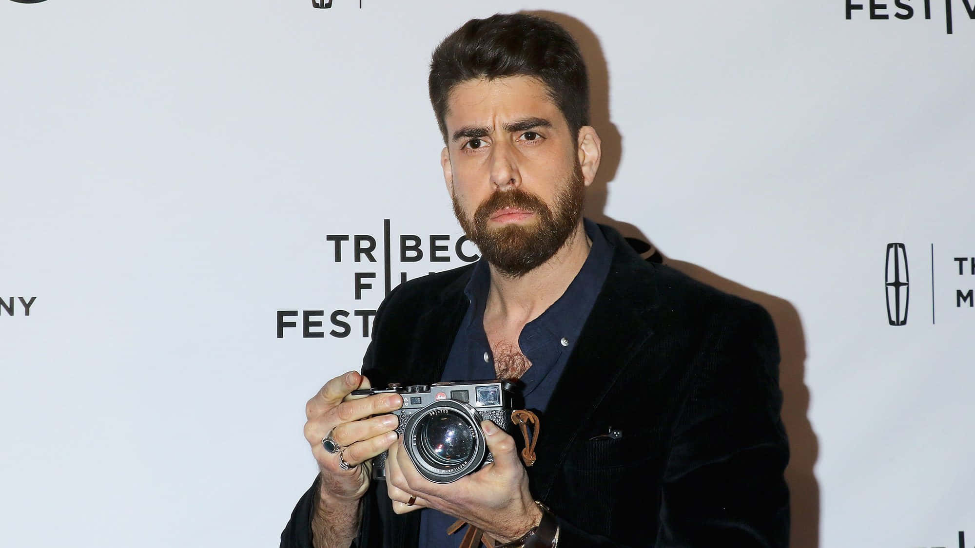 Celebrity 桌布 壁紙 — 一位留鬍鬚的男子身穿黑色天鵝絨西裝外套，在Tribeca電影節活動中手持一部復古相機。