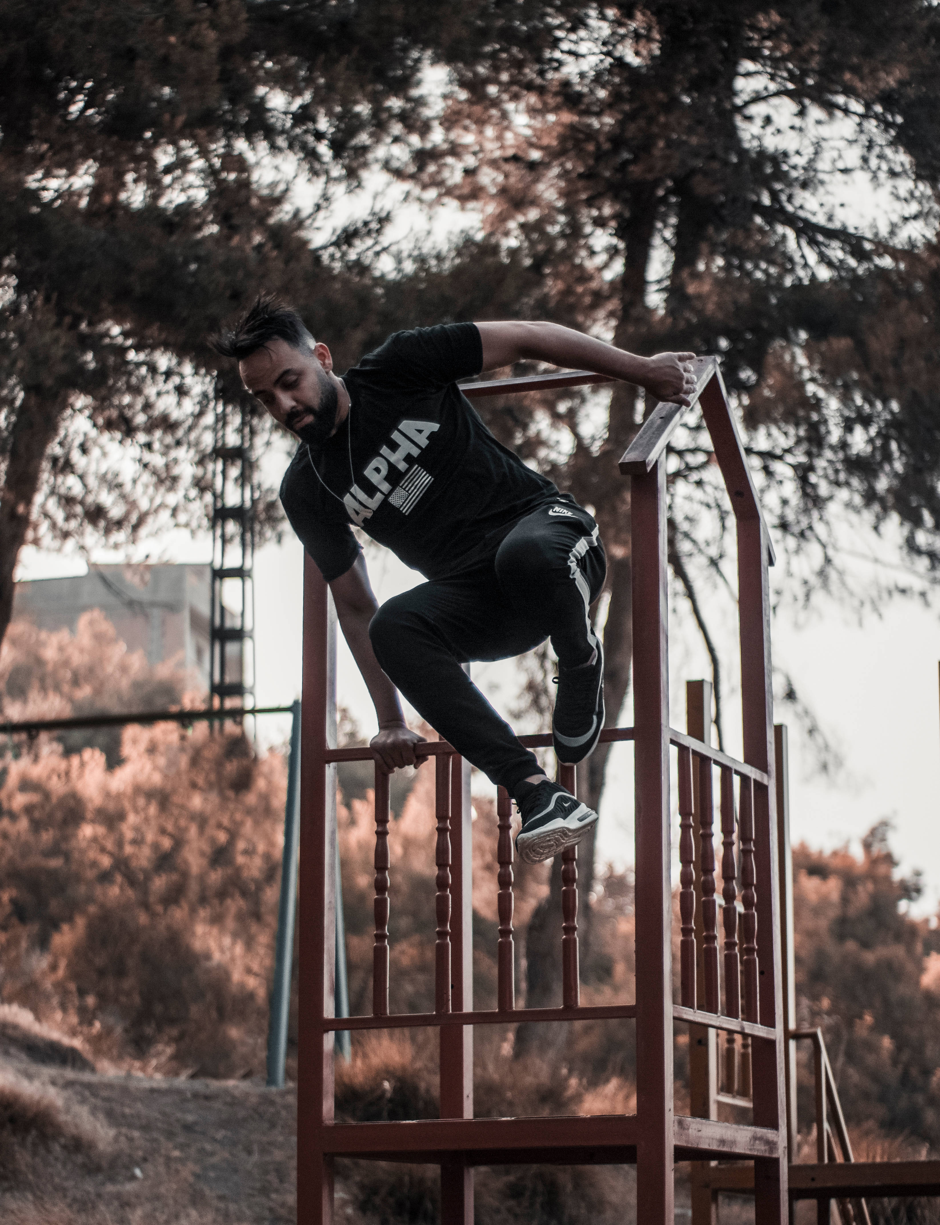 Parkour 桌布 壁紙 — 一位留鬍鬚的男子身穿黑色運動服，在黃金時段於樹林戶外區域攀爬生鏽的紅色金屬梯子。