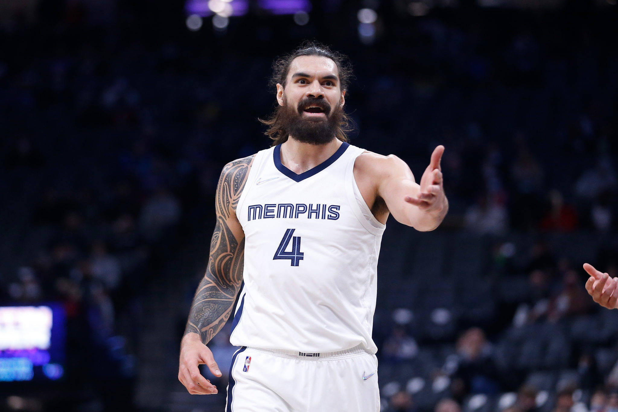 Steven Adams 桌布 壁紙 — 一位留鬍鬚的籃球運動員身穿白色曼菲斯4號球衣，在場館燈光下比賽時激烈地做手勢。