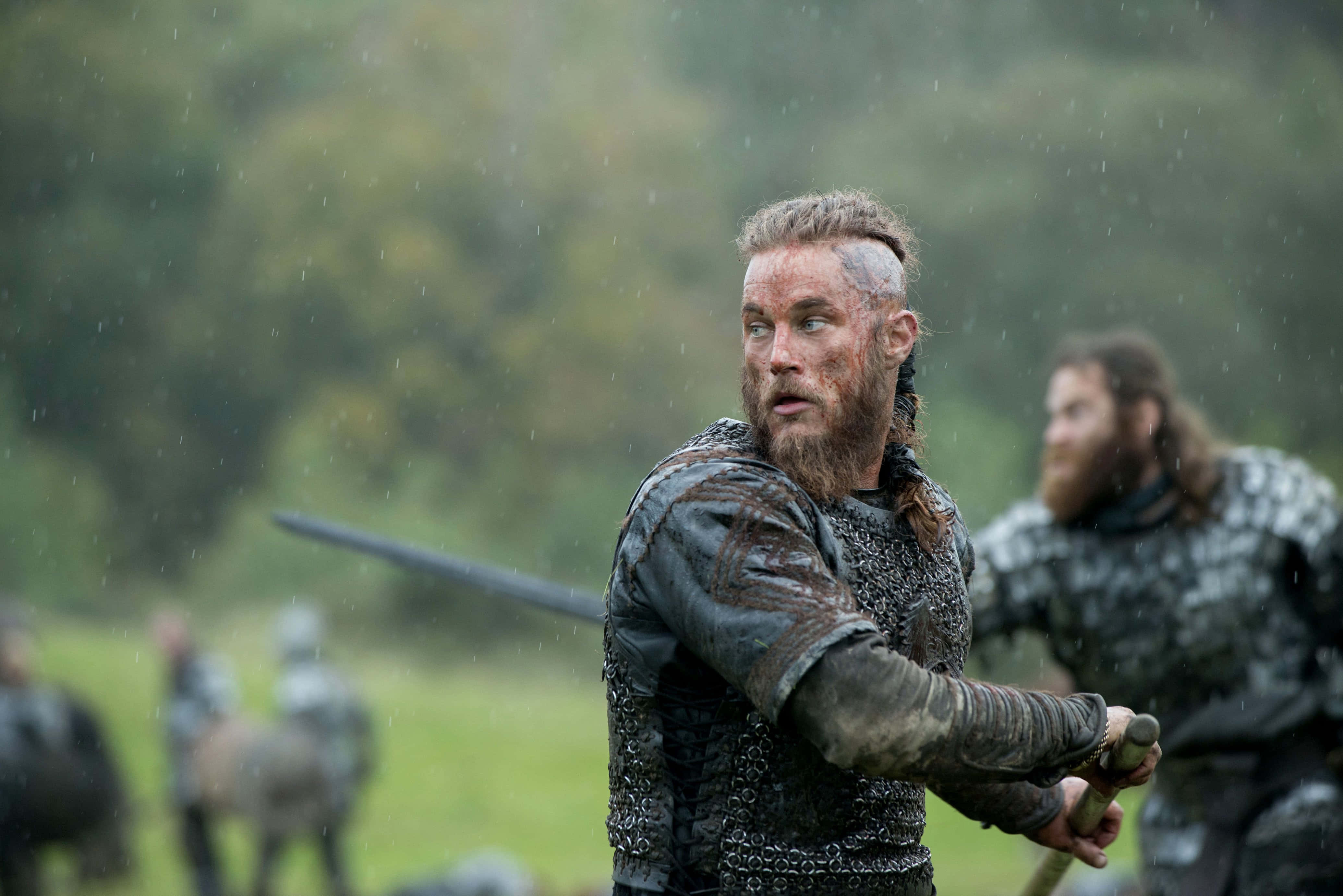 Vikings 桌布 壁紙 — 一位留鬍鬚的維京戰士身穿鎖子甲，在霧氣瀰漫的綠色田野戰鬥中，雨點落下時緊握著劍。