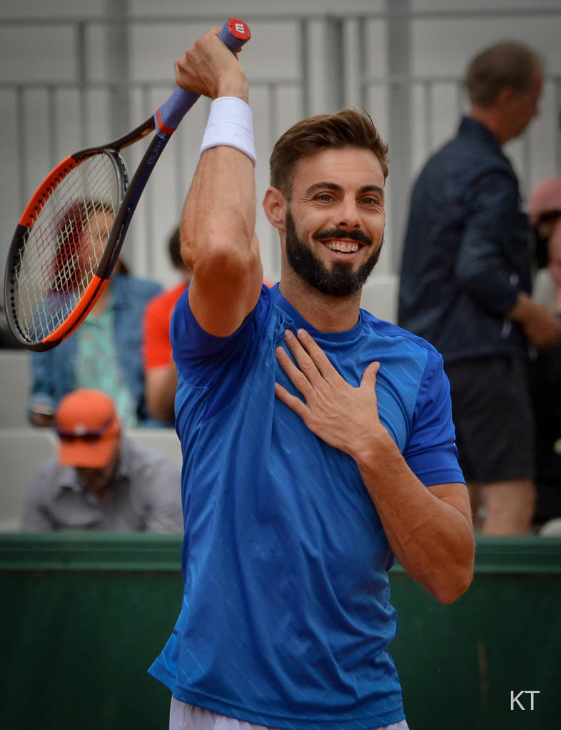 Athlete 桌布 壁紙 — 一位留鬍鬚的網球運動員身穿藍色襯衫，高舉球拍，手放在心口，露出勝利的微笑。