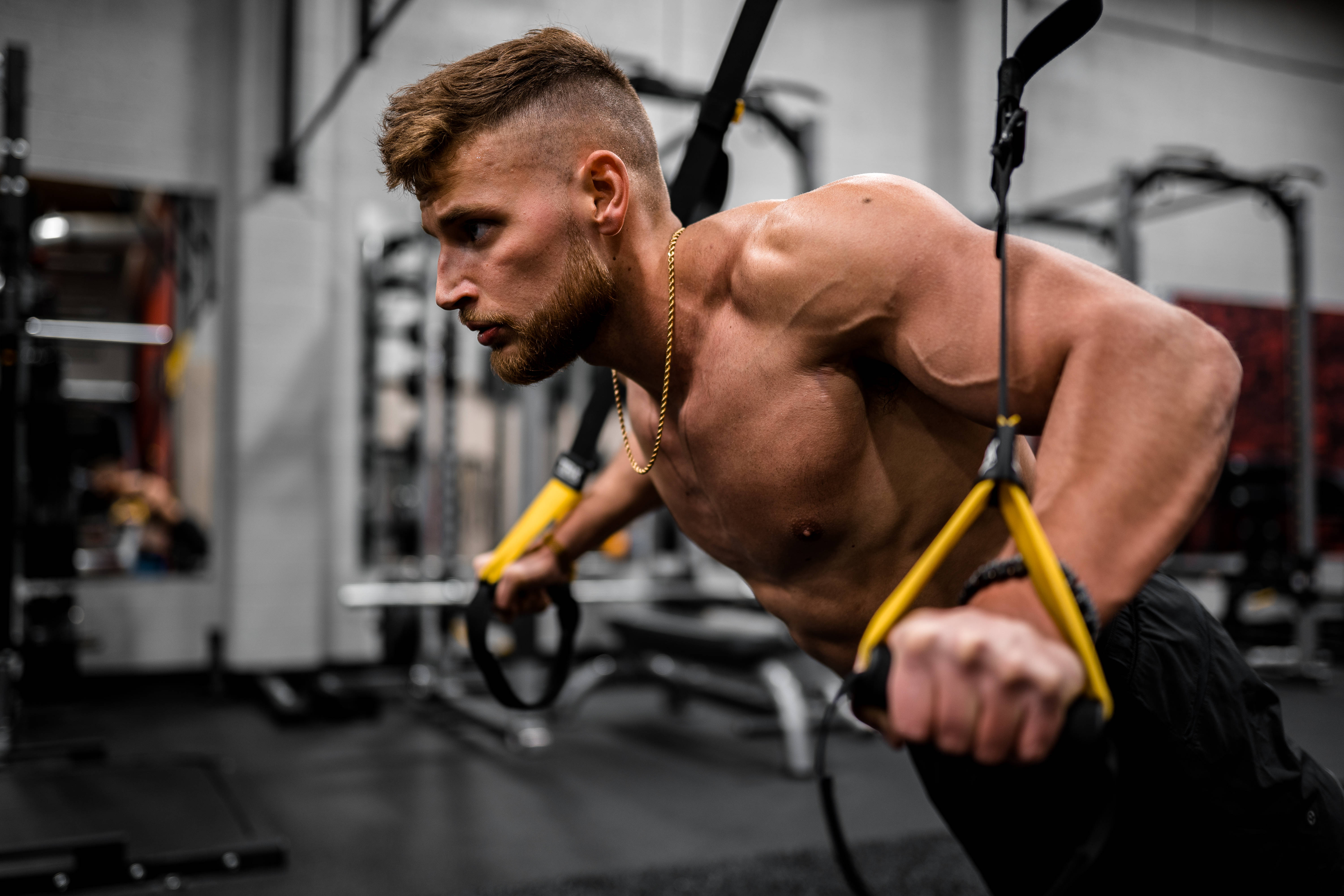 shoulder shrug 桌布 壁紙 — 一位留鬍鬚的肌肉男在現代健身房中專注地進行TRX伏地挺身。