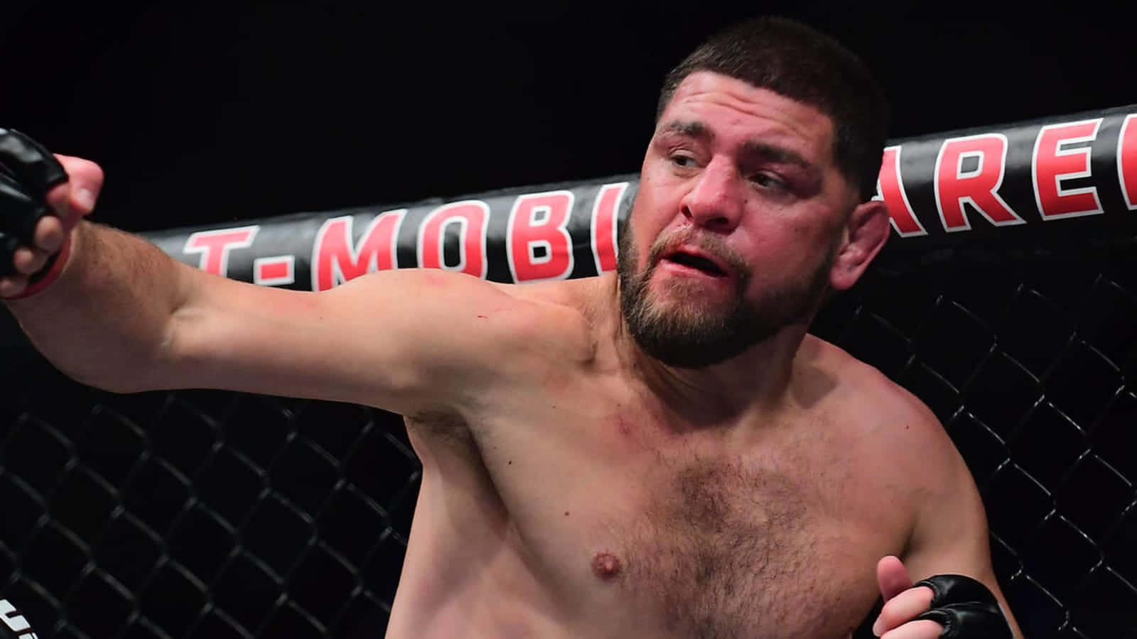UFC 桌布 壁紙 — 一位留鬍鬚的肌肉發達拳手在燈光昏暗的MMA八角籠內揮拳，T-Mobile Arena標誌清晰可見。