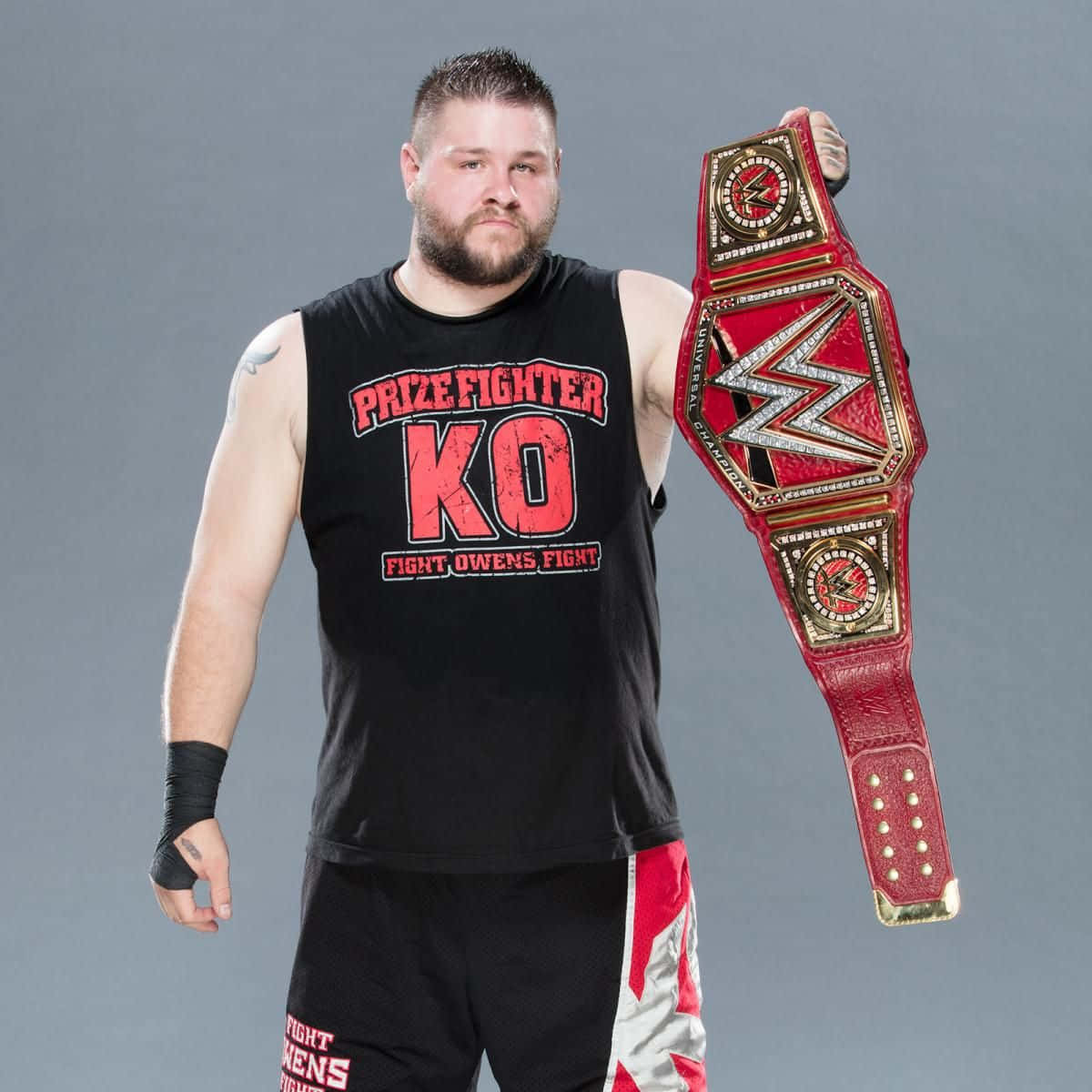 WWE 桌布 壁紙 — 一位留鬍鬚的肌肉發達摔角手，身穿印有紅色文字的黑色背心，手持紅金冠軍腰帶。