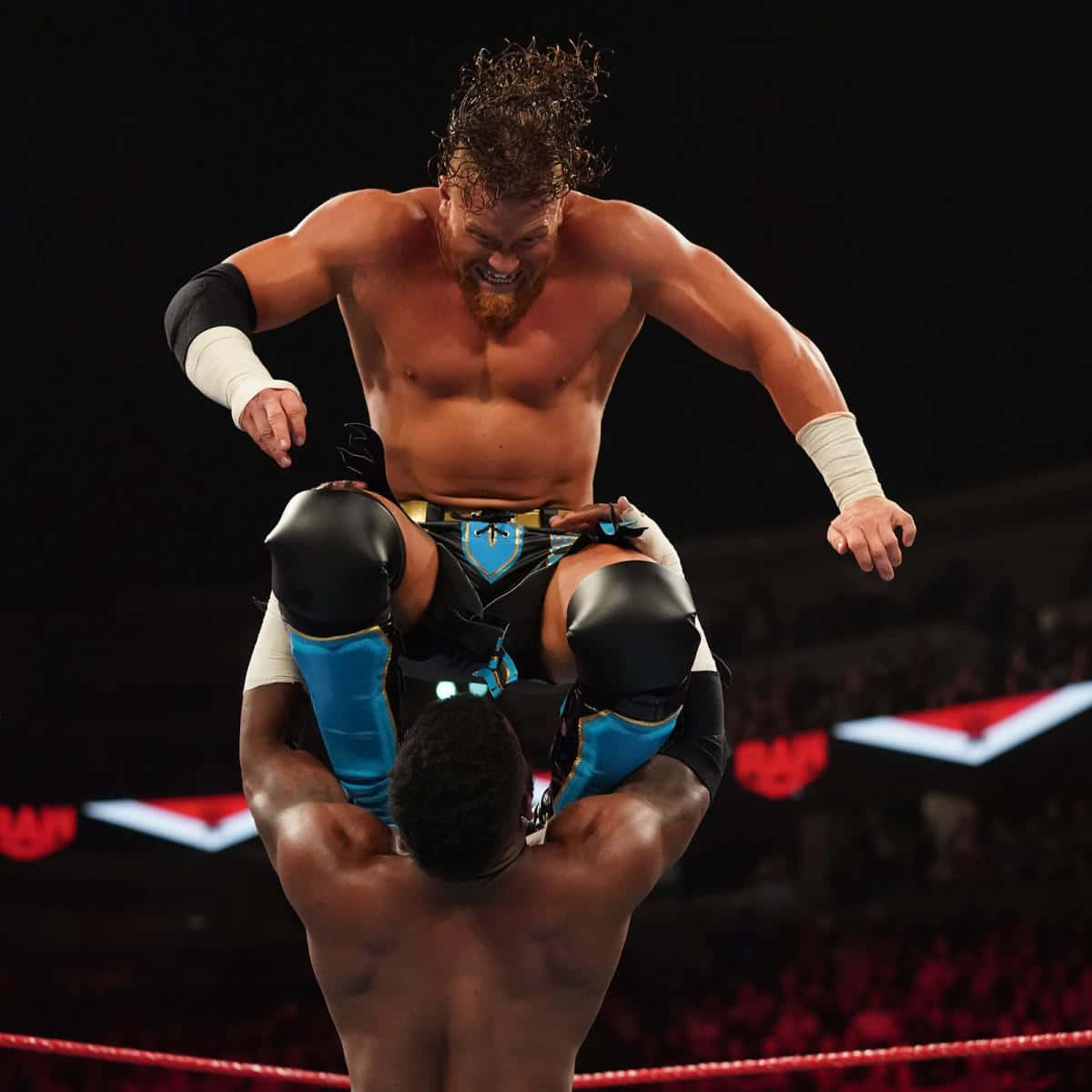 WWE 桌布 壁紙 — 一位留鬍鬚的肌肉發達摔角手在明亮的場館燈光下，於摔角擂台內將另一位摔角手高舉過頭。