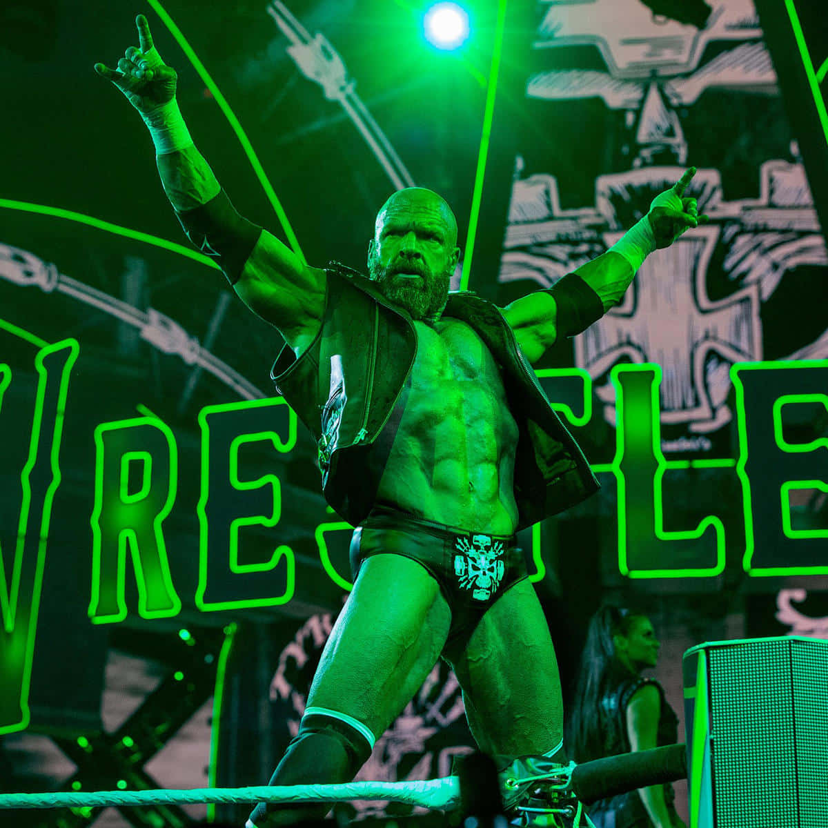WWE 桌布 壁紙 — 一位留鬍鬚的肌肉發達摔角手在綠色燈光下的擂台上勝利地站著，高舉雙臂慶祝勝利。