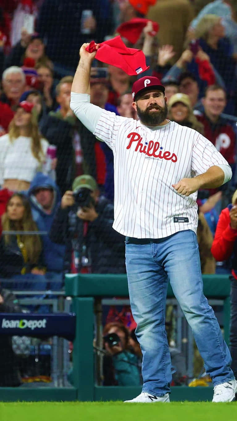 Jason Kelce 桌布 壁紙 — 一位留鬍鬚的費城人隊棒球選手在夜晚向歡呼的球迷揮動他的紅色帽子。