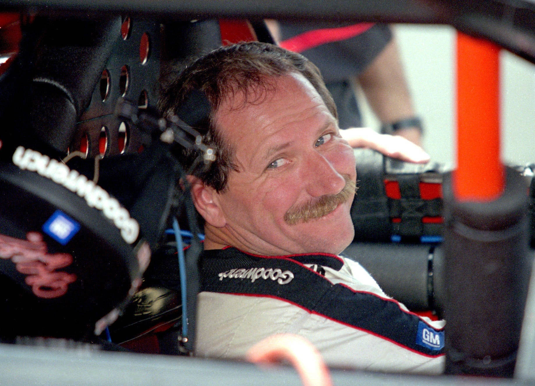 Dale Earnhardt 桌布 壁紙 — 一位留鬍鬚的賽車手微笑著從駕駛艙向外望，身穿GoodYear品牌的賽車服。