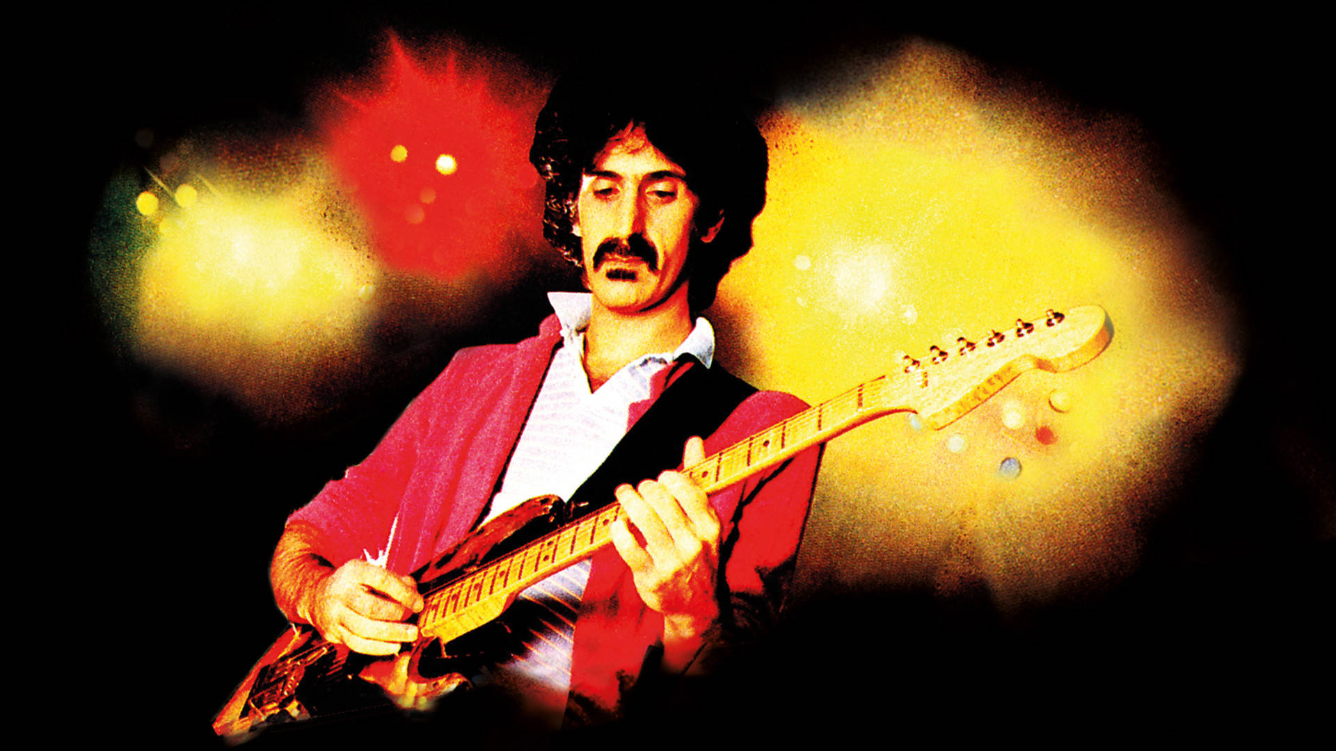Zappa 桌布 壁紙 — 一位留鬍鬚的音樂家在黑暗背景下，於充滿活力的舞台燈光下彈奏紅色電吉他。