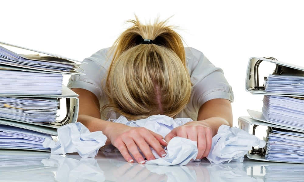 Woman 桌布 壁紙 — 一位疲倦的金髮女子將頭靠在雜亂的桌子上，周圍堆滿了高聳的文件和皺巴巴的紙張。