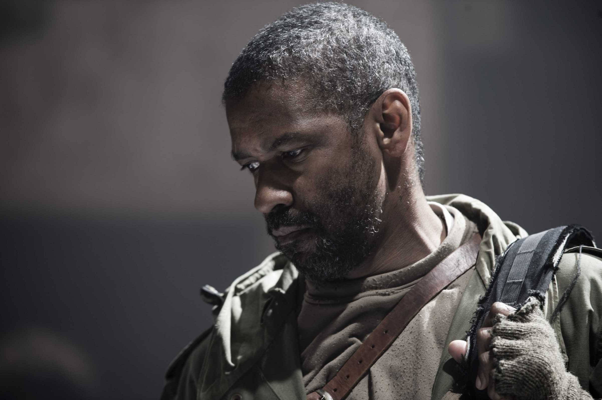 Denzel Washington 桌布 壁紙 — 一位疲憊的士兵，留著灰白鬍鬚，身穿戰術裝備，在昏暗骯髒的環境中向下凝視。
