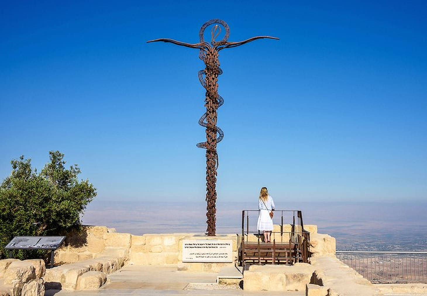 Jordan 桌布 壁紙 — 一位白衣女子站在石頭觀景台上，凝視著一座高大的生鏽金屬雕塑，背景是廣闊的藍天。