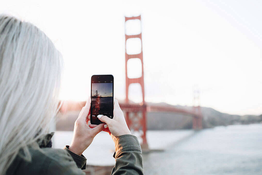 photography iPhone 桌布 壁紙 — 一位白髮人士透過智慧型手機捕捉日落時分的金門大橋。