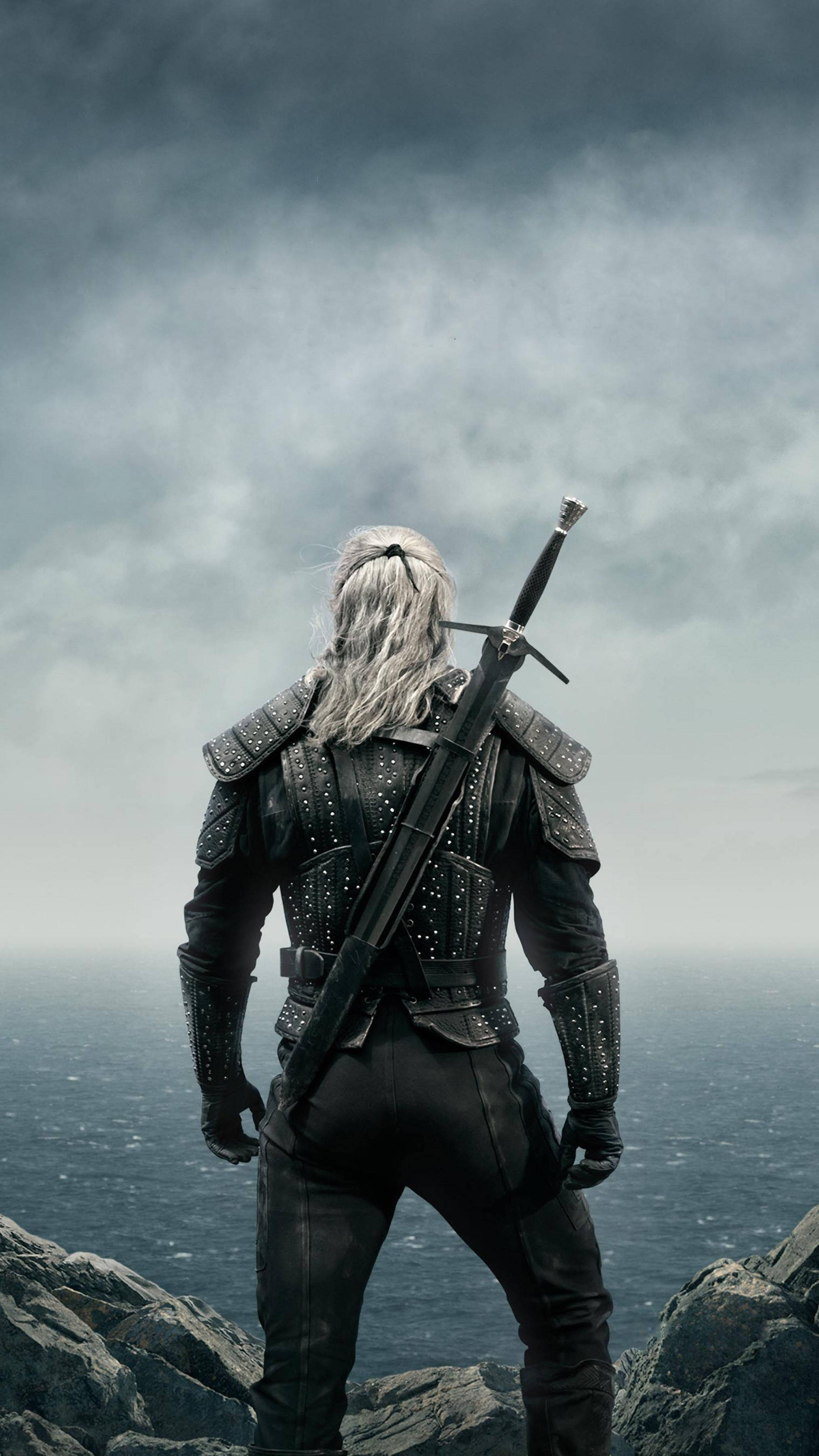 Witcher 桌布 壁紙 — 一位白髮孤獨戰士手持劍，站在岩石峭壁上，俯瞰灰色天空下的暴風雨海洋。