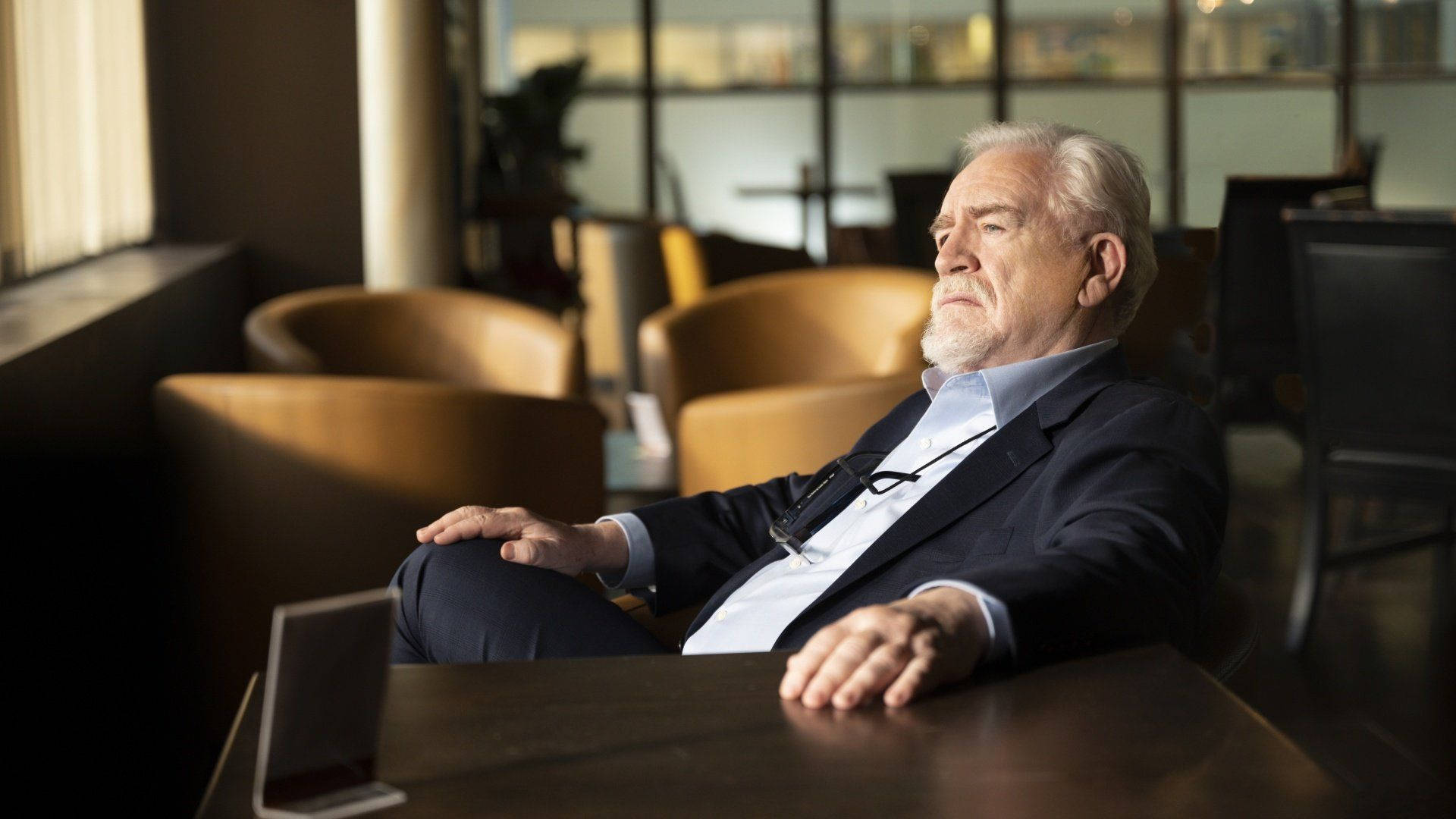 Succession 桌布 壁紙 — 一位白髮年長男士悠閒地坐在現代咖啡館內，陽光從他身後的窗戶灑進來。