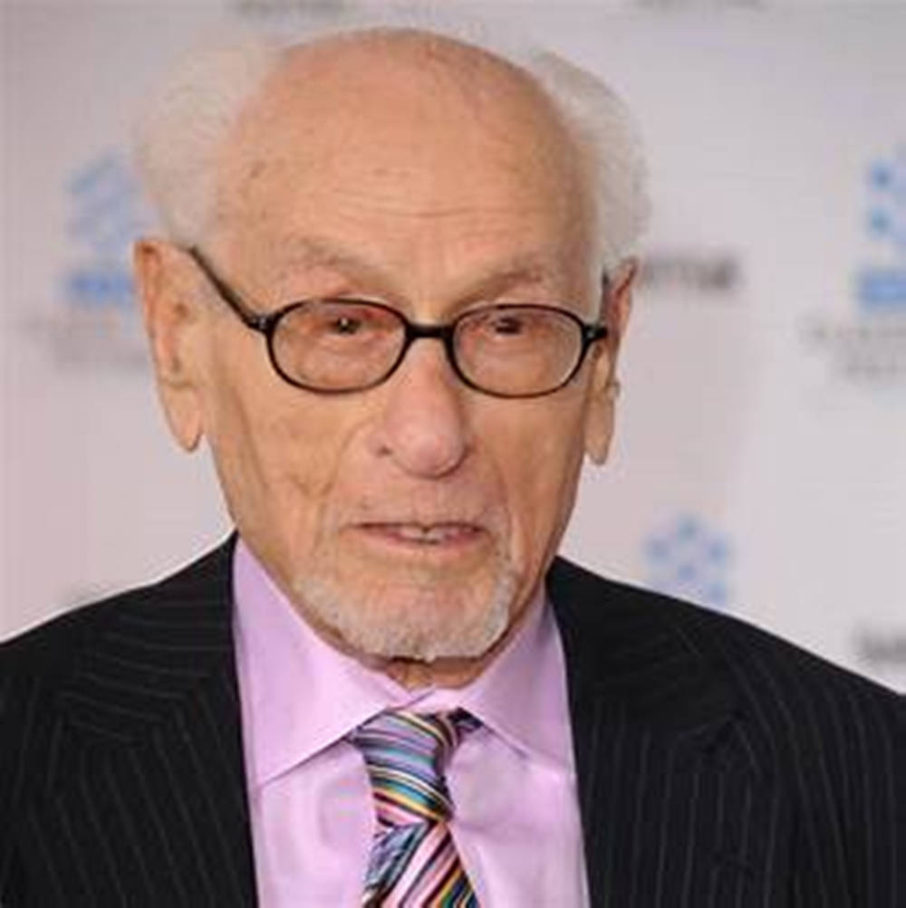 Celebrity 桌布 壁紙 — 一位白髮戴眼鏡的長者，穿著細條紋西裝和彩色條紋領帶，背景是模糊的活動場景。