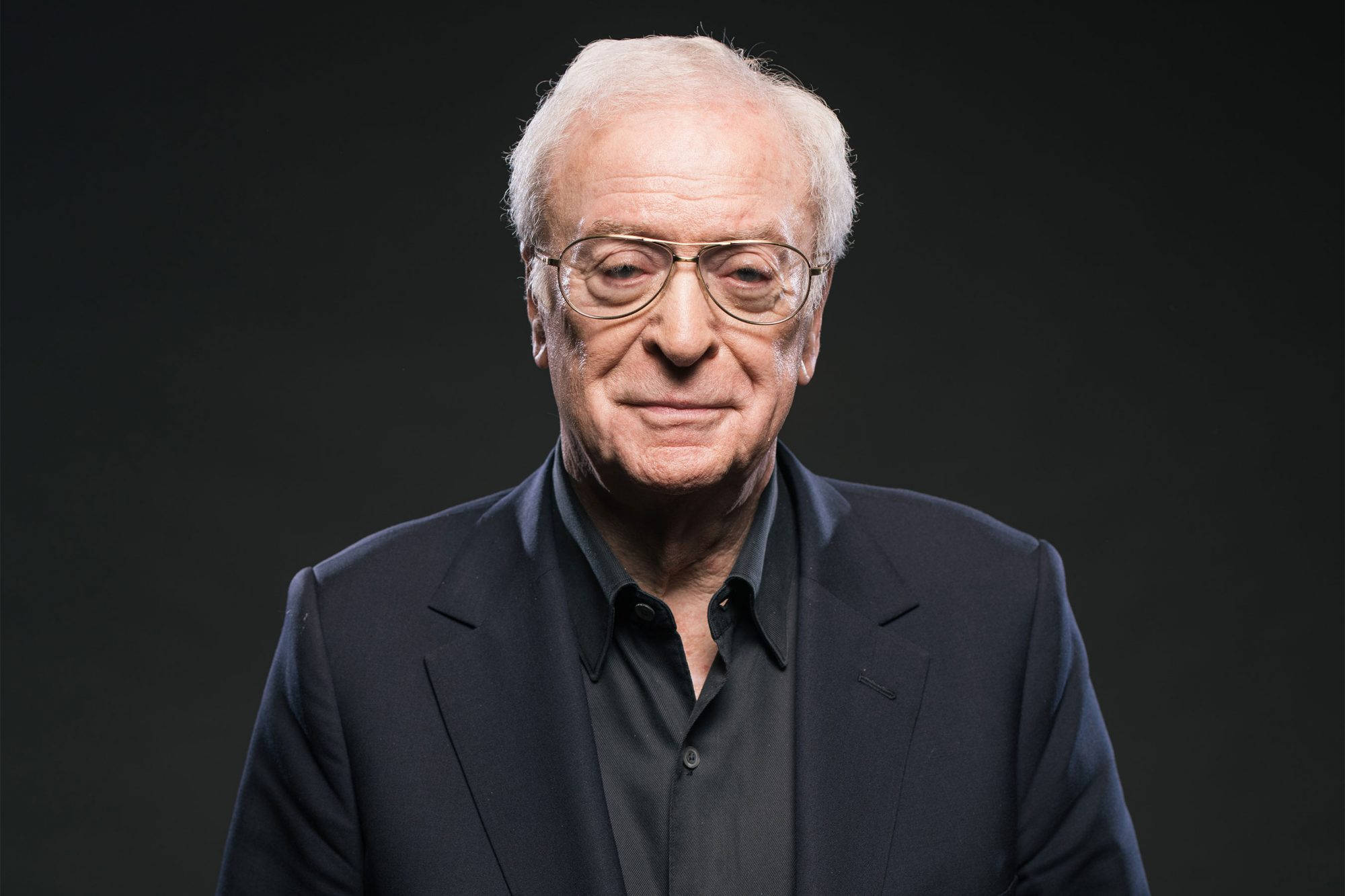 actor 桌布 壁紙 — 一位白髮戴眼鏡的長者，身穿深色西裝，背景為黑色。