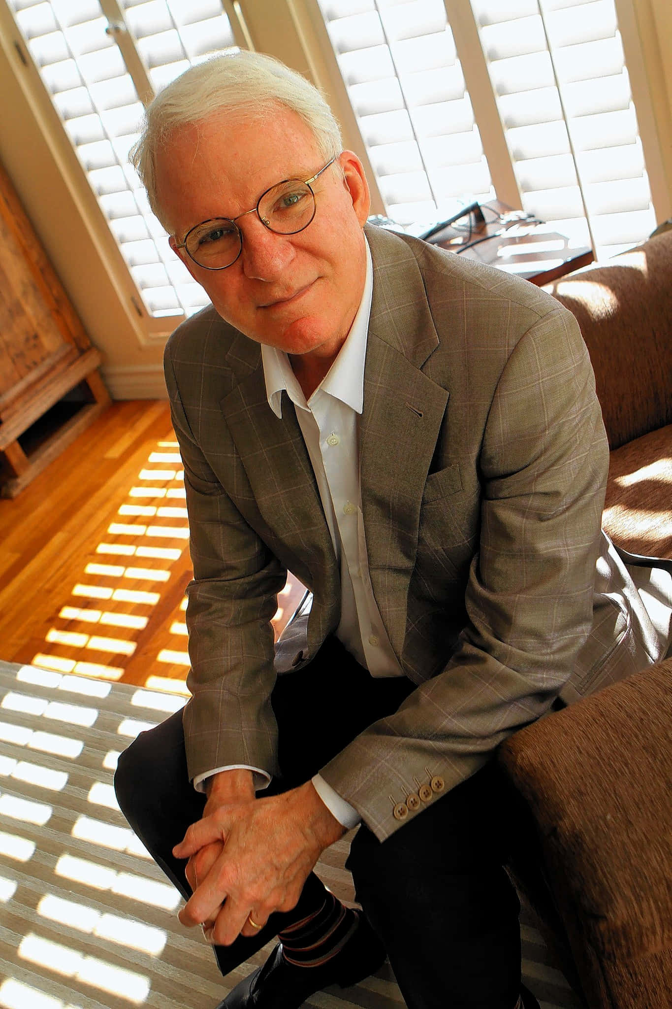 steve martin 桌布 壁紙 — 一位白髮戴眼鏡的長者坐在沙發上，房間陽光充足，木地板和百葉窗投射出條紋狀陰影。