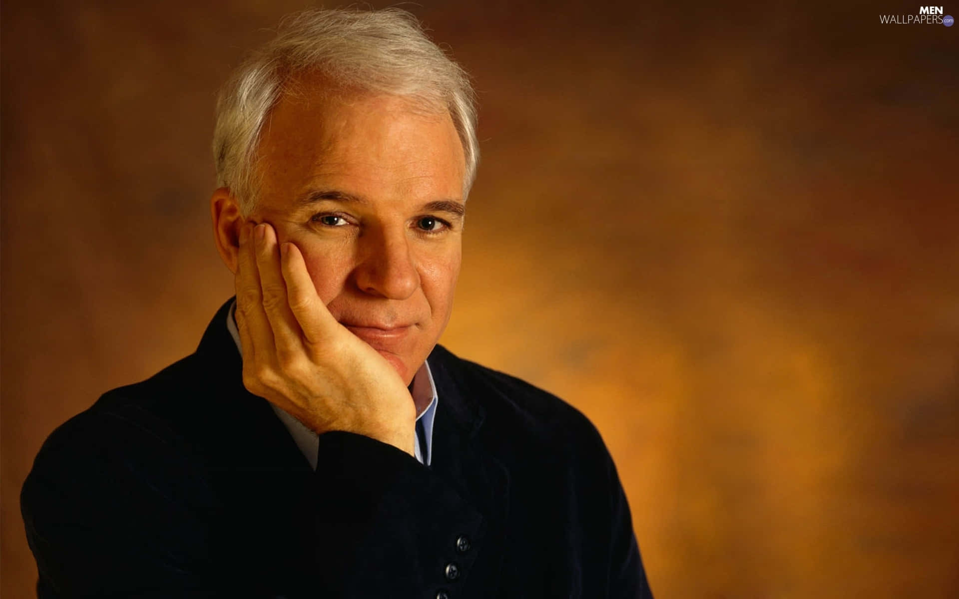 steve martin 桌布 壁紙 — 一位白髮沉思的男子，在溫暖的漸層背景前，用手托著下巴。