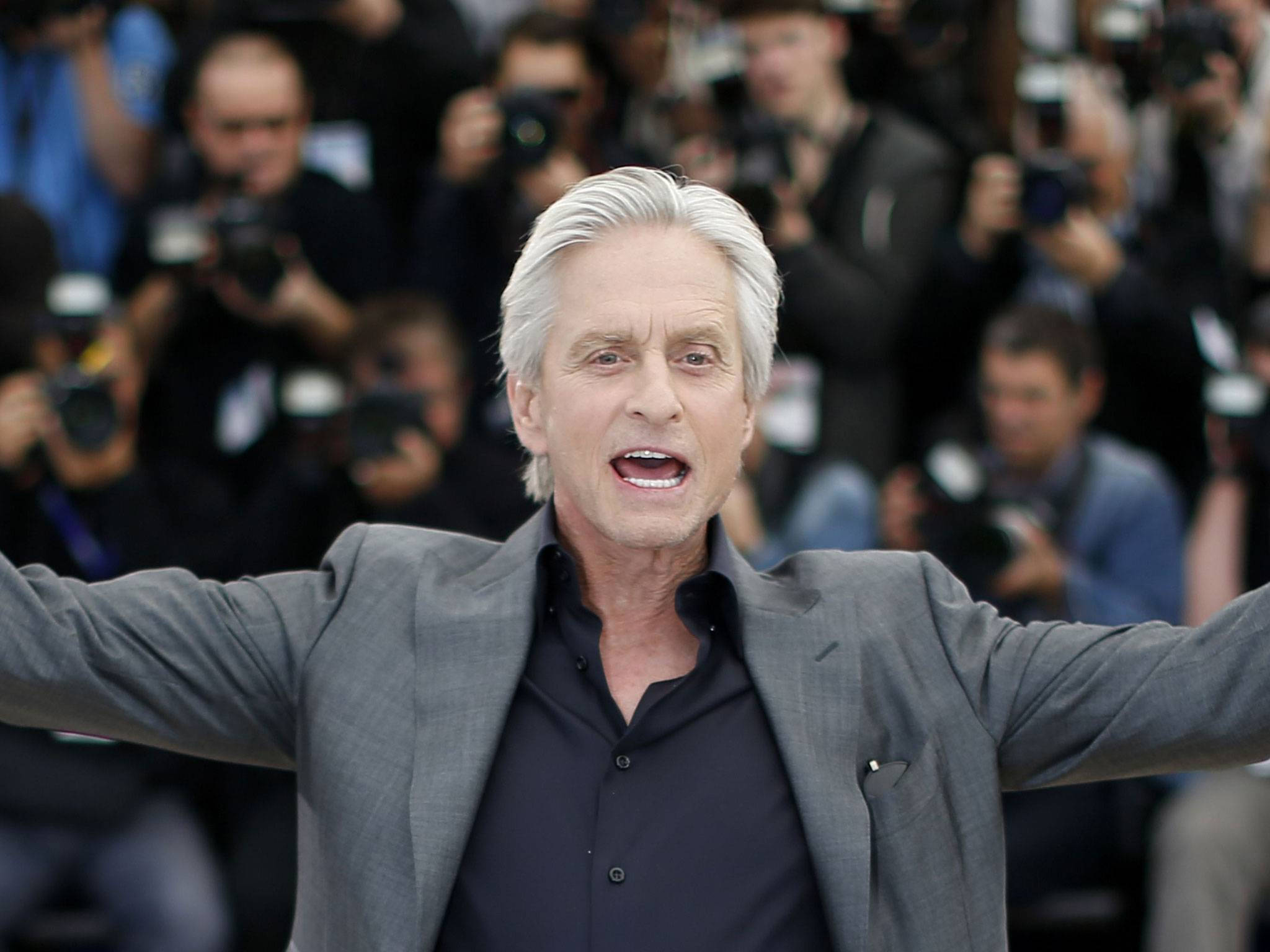 actor 桌布 壁紙 — 一位白髮男士身穿灰色西裝，雙臂張開站立，身後有攝影師在拍照。