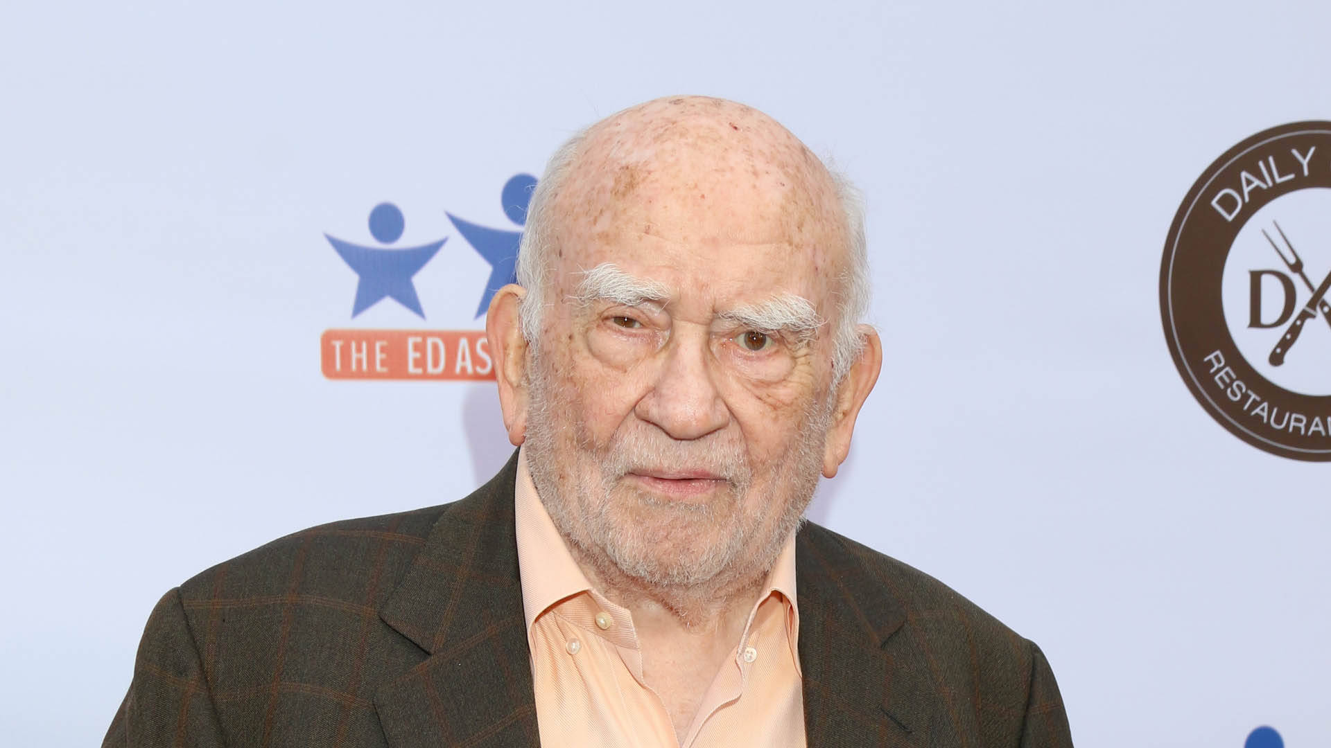 白色美學動圖 桌布 壁紙 — 一位白髮白鬍子的長者穿著棕色格紋西裝和桃色襯衫，背景是淺藍色的活動背景。