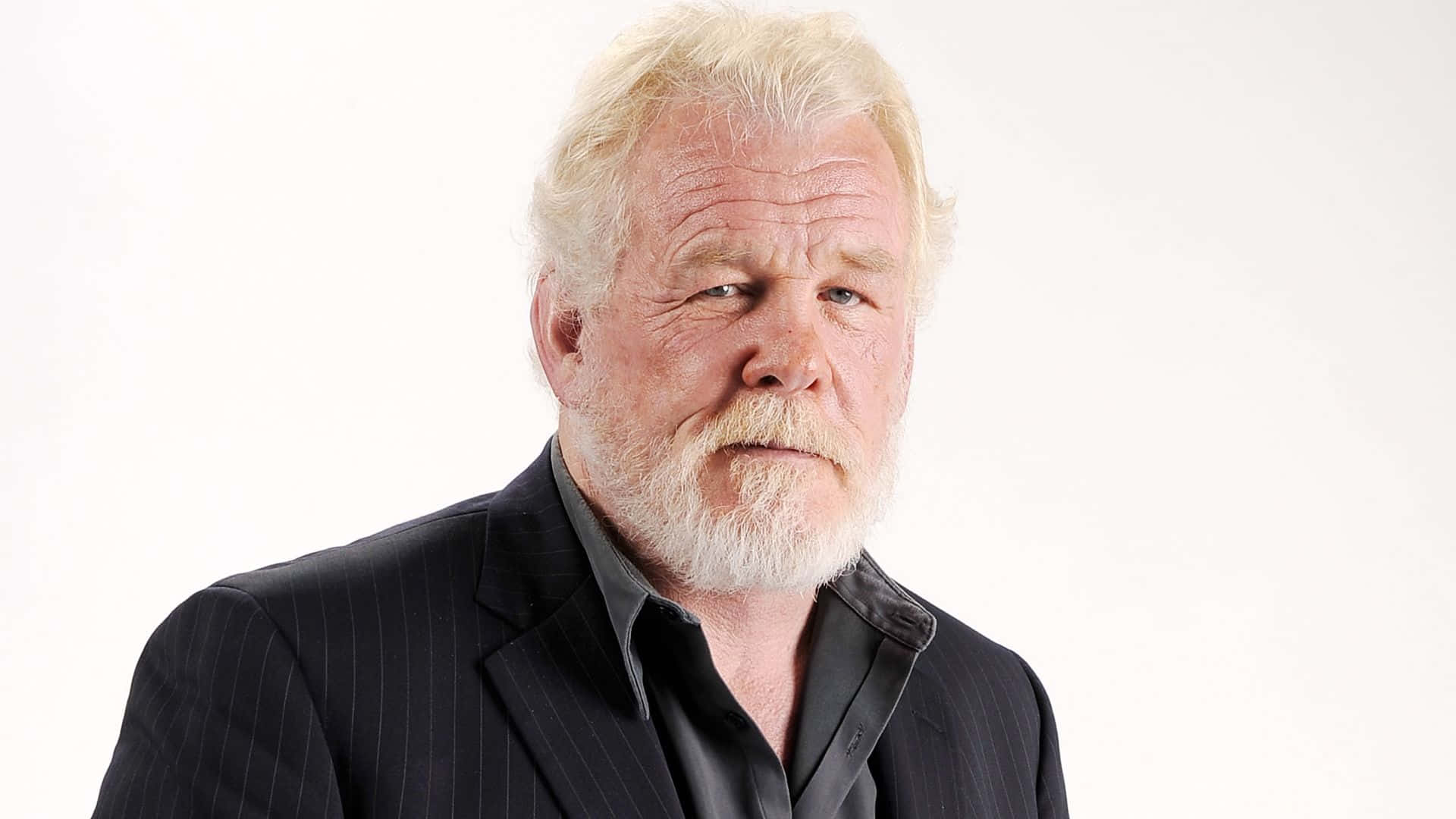 Nick Nolte 桌布 壁紙 — 一位白髮白鬍鬚男士的近距離肖像，身穿深色細條紋西裝，背景為純白色。