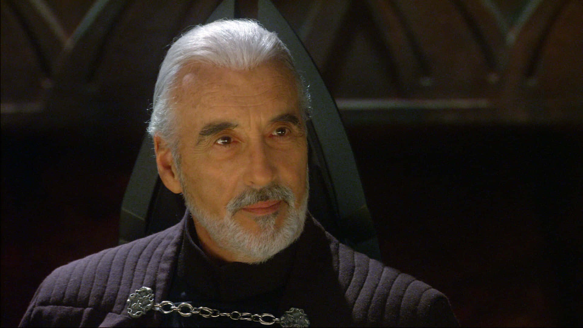 Count Dooku 桌布 壁紙 — 一位白髮白鬍鬚的男人穿著深色長袍，戴著銀鏈項鍊的特寫。