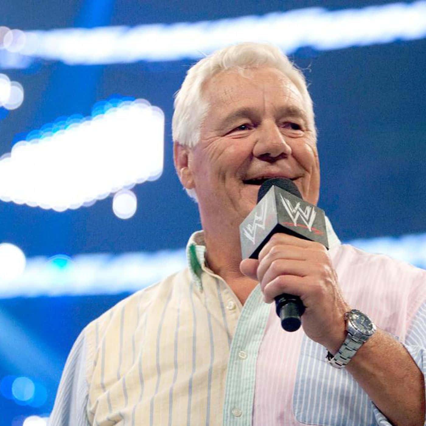 WWE 桌布 壁紙 — 一位白髮老人在明亮的藍色舞台燈光下微笑著手持WWE麥克風。