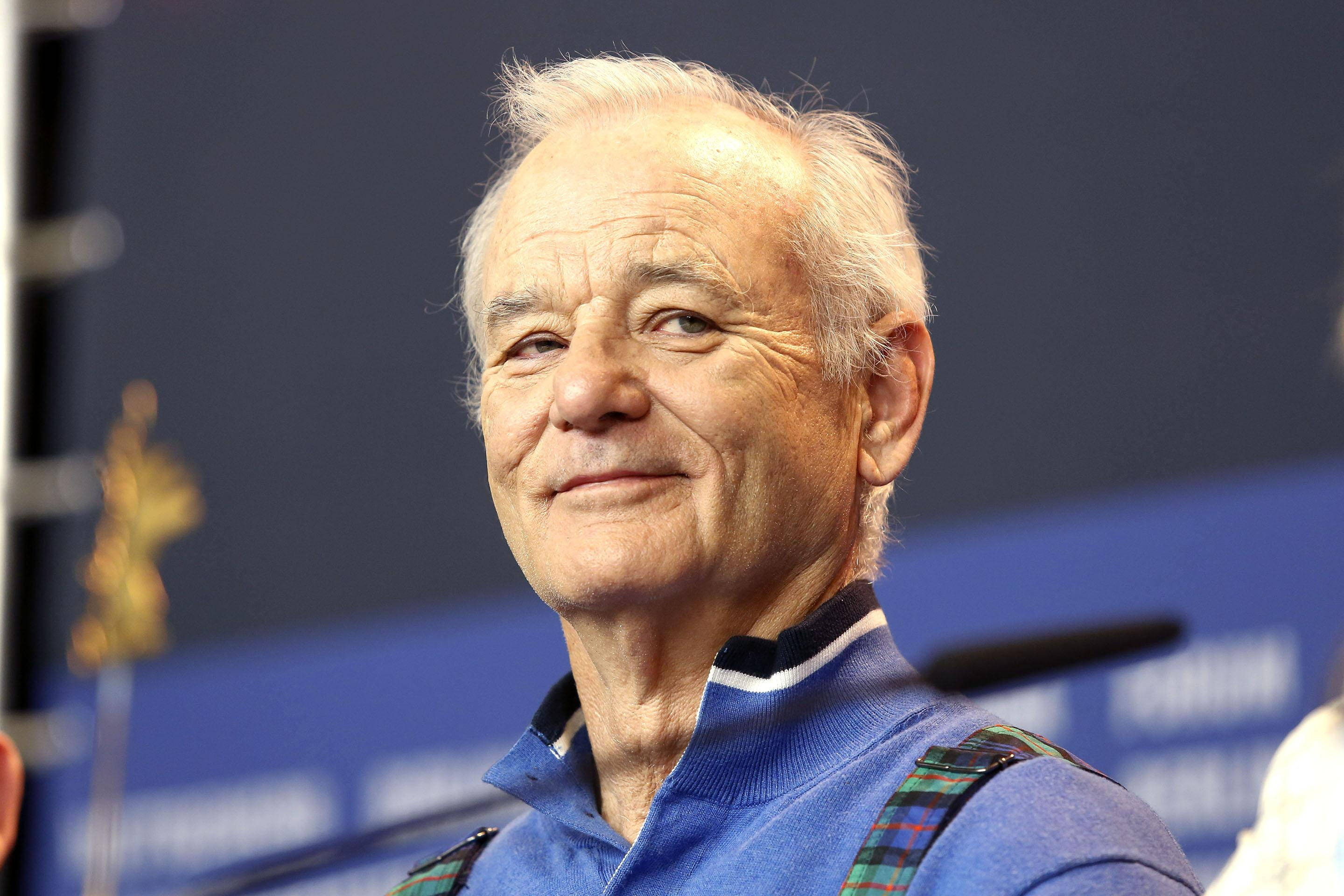 Celebrity 桌布 壁紙 — 一位白髮老人穿著藍色毛衣和格子吊帶褲，溫暖地微笑。