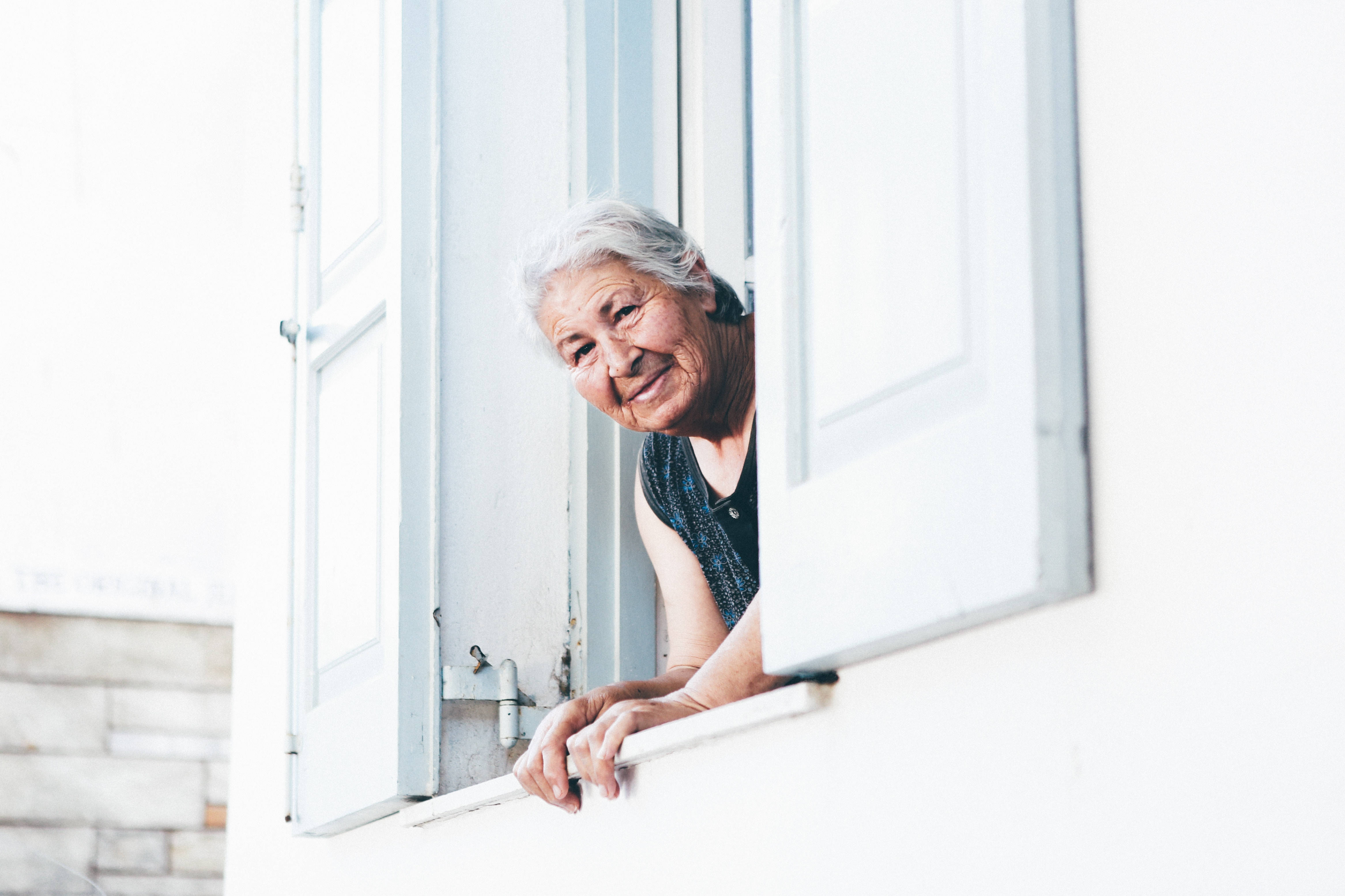 Woman 桌布 壁紙 — 一位白髮老婦人從白色窗框探出頭來，露出溫暖的笑容。