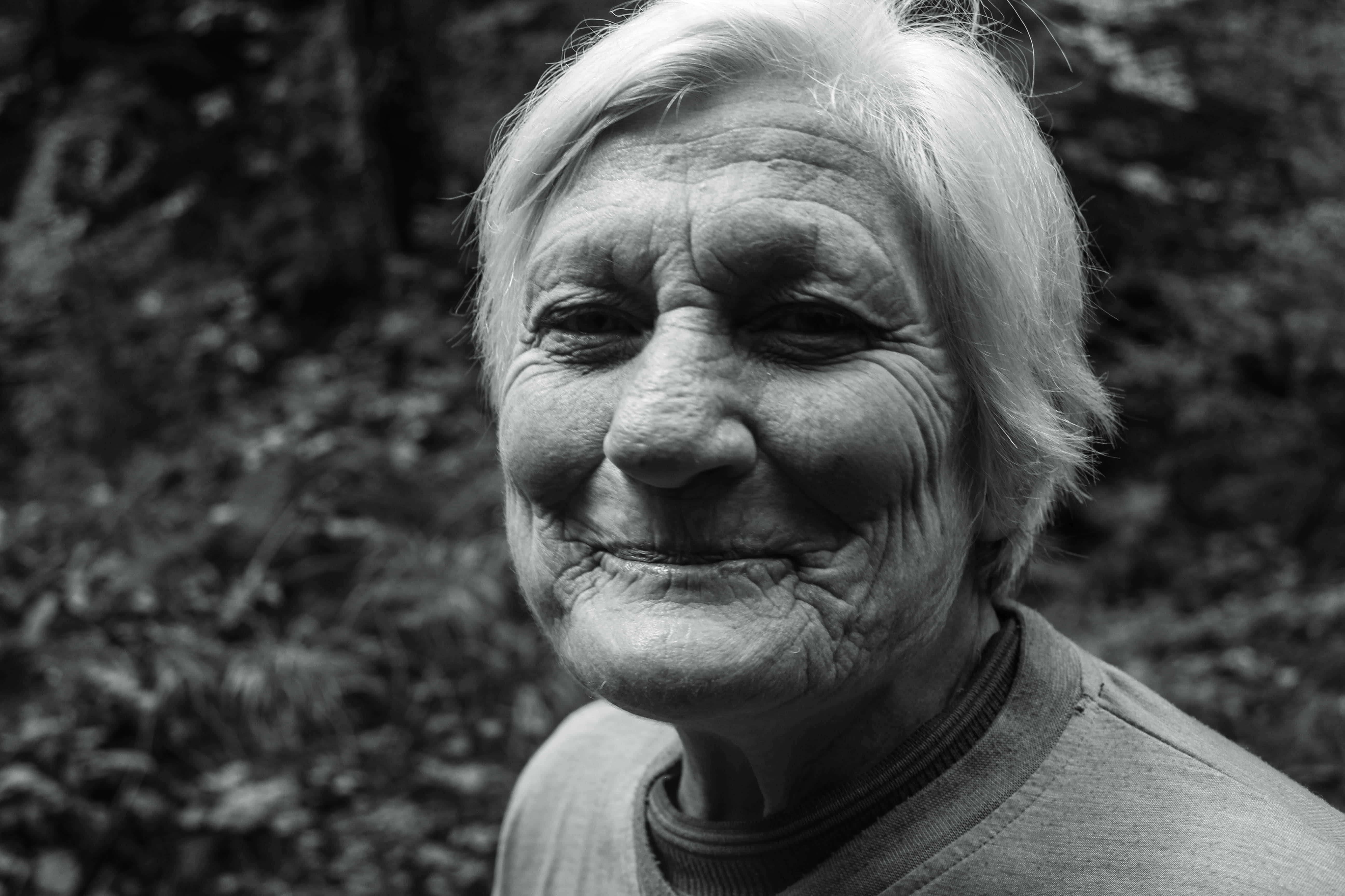 Smile 桌布 壁紙 — 一位白髮老婦在森林環境中溫暖微笑的黑白特寫肖像。