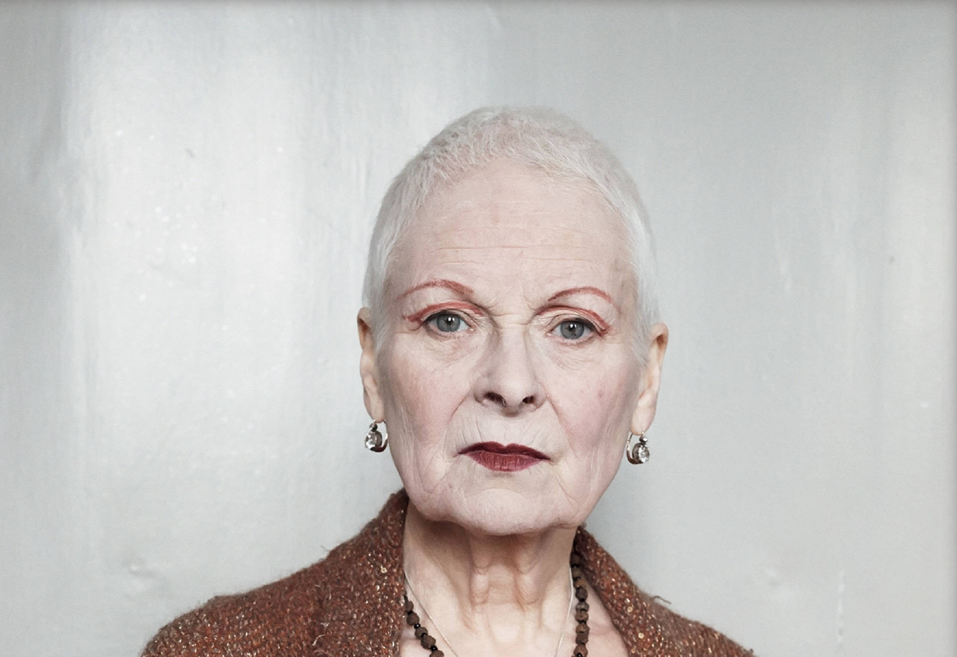 Vivienne Westwood 桌布 壁紙 — 一位白髮蒼蒼、化著大膽紅色眼妝的老婦人，在純白牆壁前的特寫肖像。