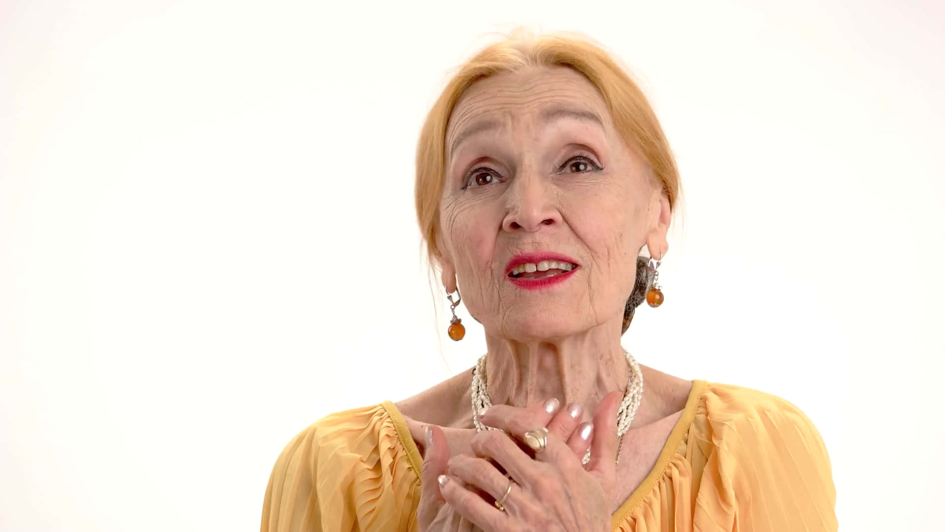 Old Lady 桌布 壁紙 — 一位白髮蒼蒼、塗著紅色唇膏的年長女性，在純白背景前將雙手交握於頸部附近。