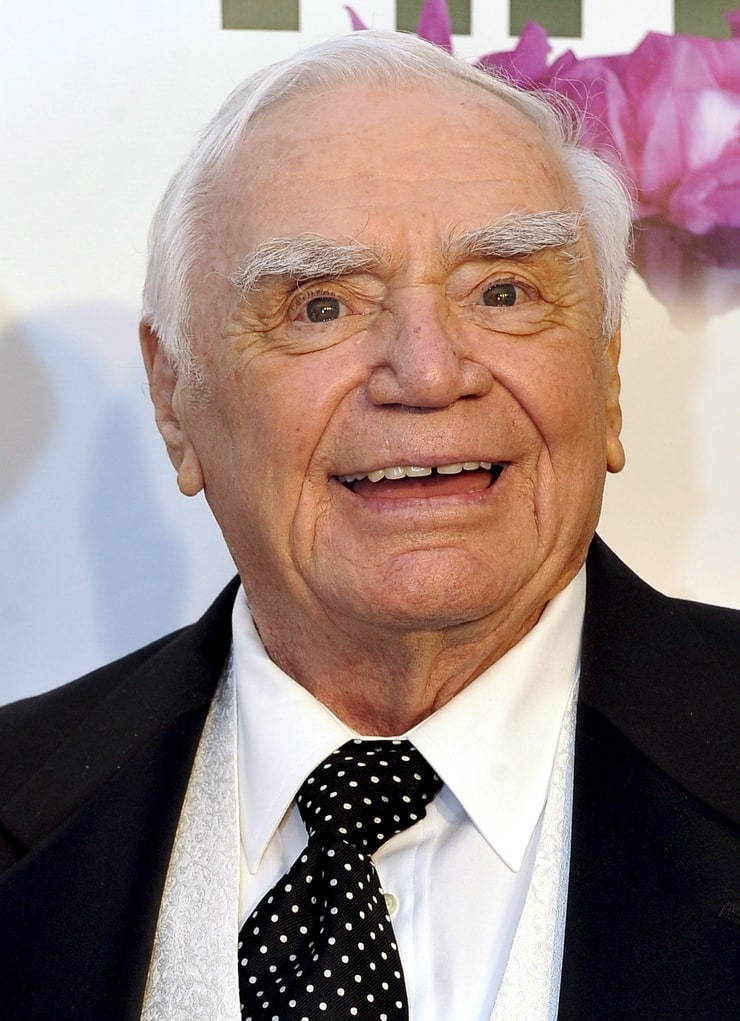 actor 桌布 壁紙 — 一位白髮蒼蒼、笑容滿面的長者，身穿黑色西裝和波點領帶，背景是花卉圖案。