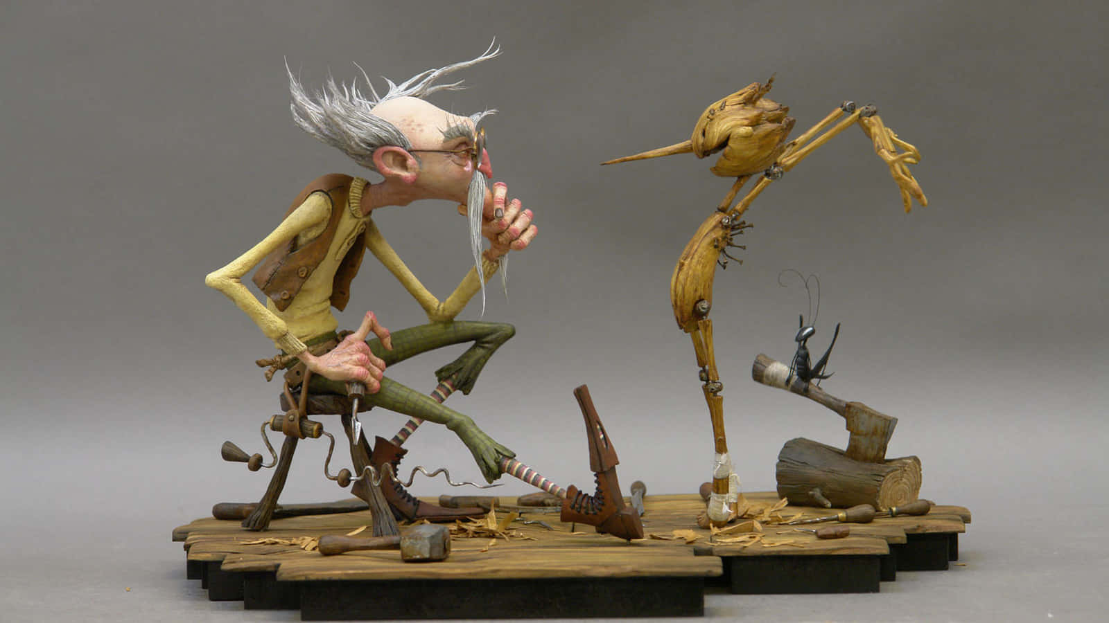 Guillermo Del Toro's Pinocchio 桌布 壁紙 — 一位白髮蓬鬆、戴著眼鏡的年長木雕工匠，坐在凳子上精心雕刻一隻奇特的木鳥。