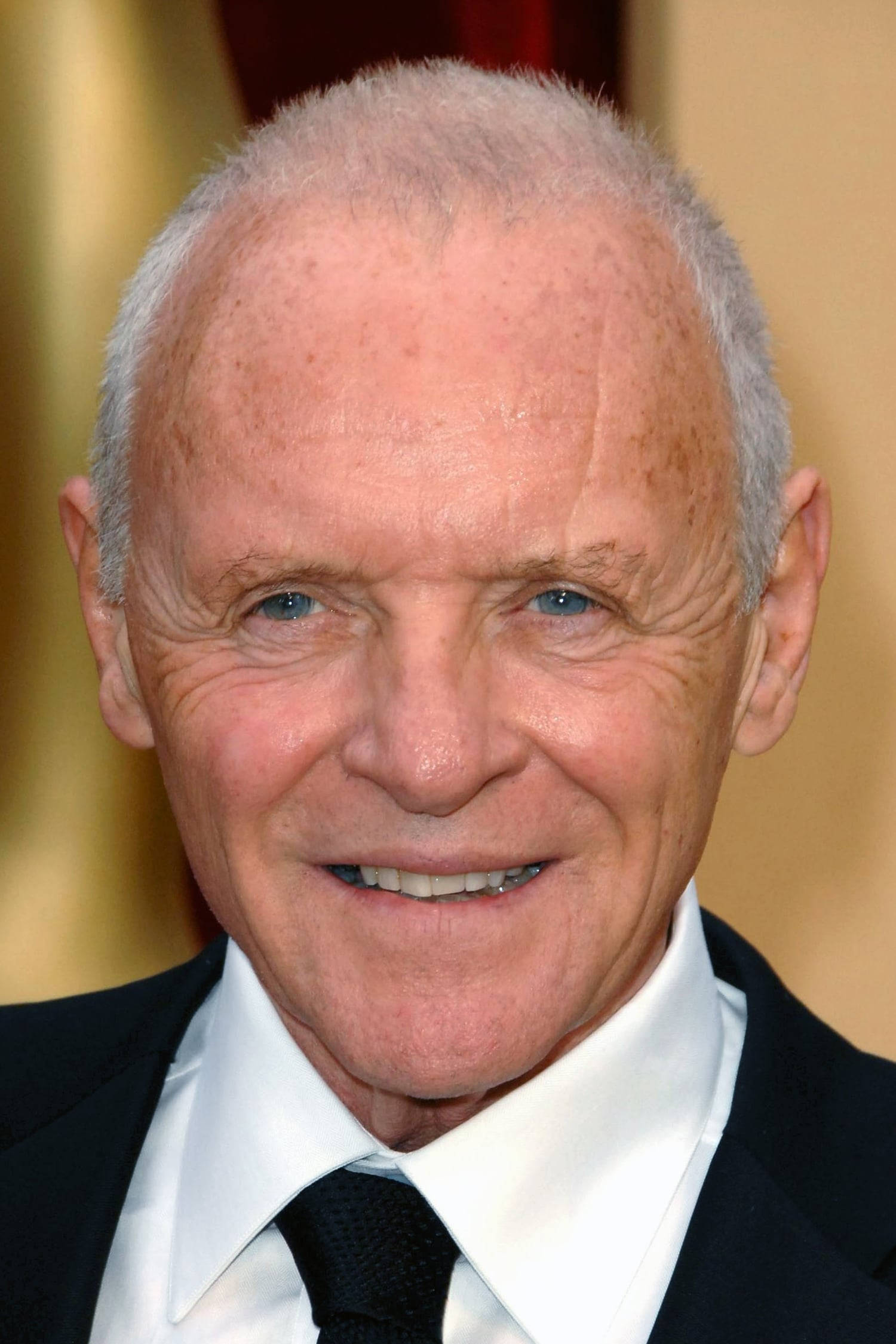 actor 桌布 壁紙 — 一位白髮藍眼的長者身穿黑色西裝打領帶，在金色背景下溫暖微笑的特寫肖像。