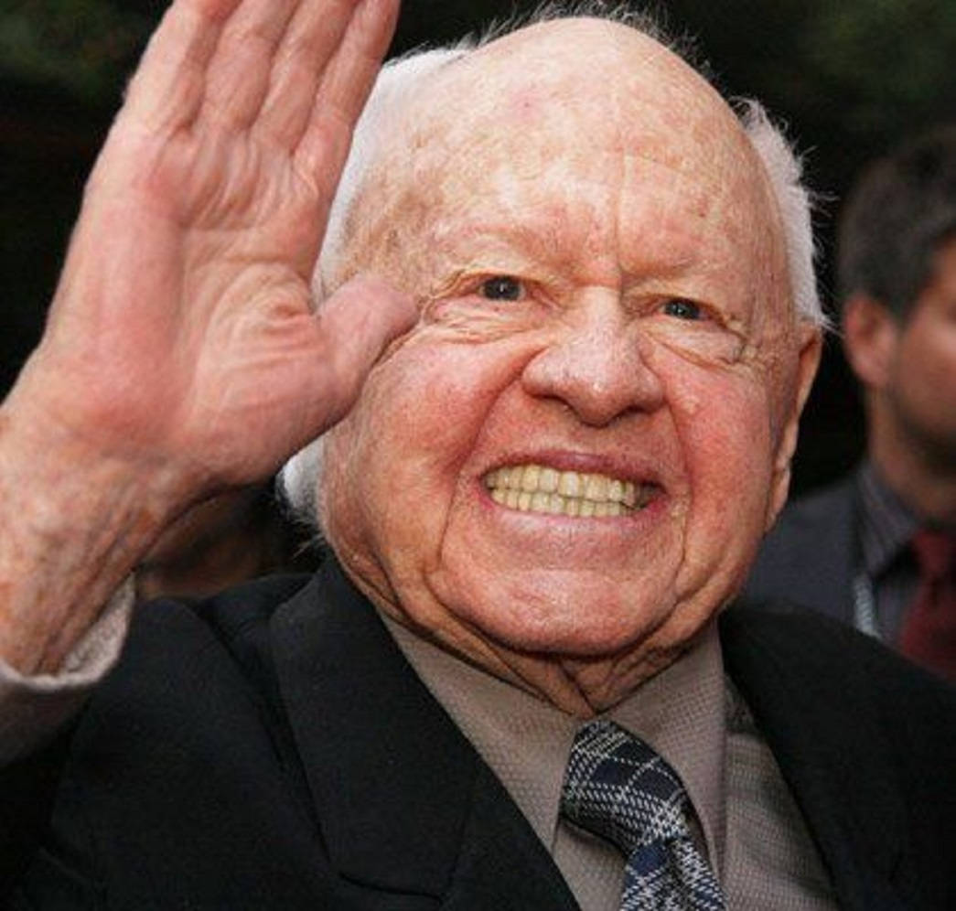 mickey rooney 桌布 壁紙 — 一位白髮長者穿著深色西裝和圖案領帶，愉快地揮手。