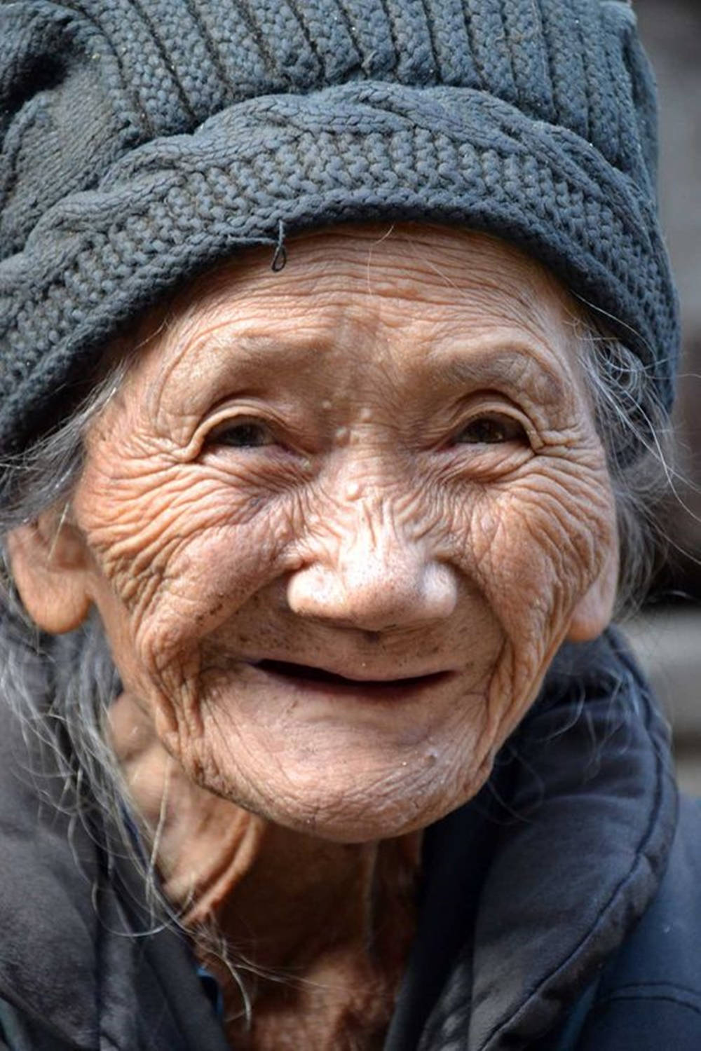 smiling 桌布 壁紙 — 一位皮膚深皺的老婦人戴著灰色針織帽，溫暖微笑的特寫肖像。