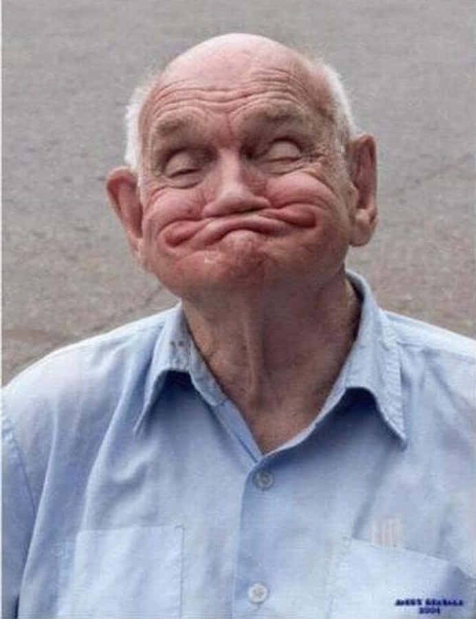 meme 桌布 壁紙 — 一位皮膚皺紋、帶著頑皮笑容的長者，在純灰色背景前瞇起眼睛。
