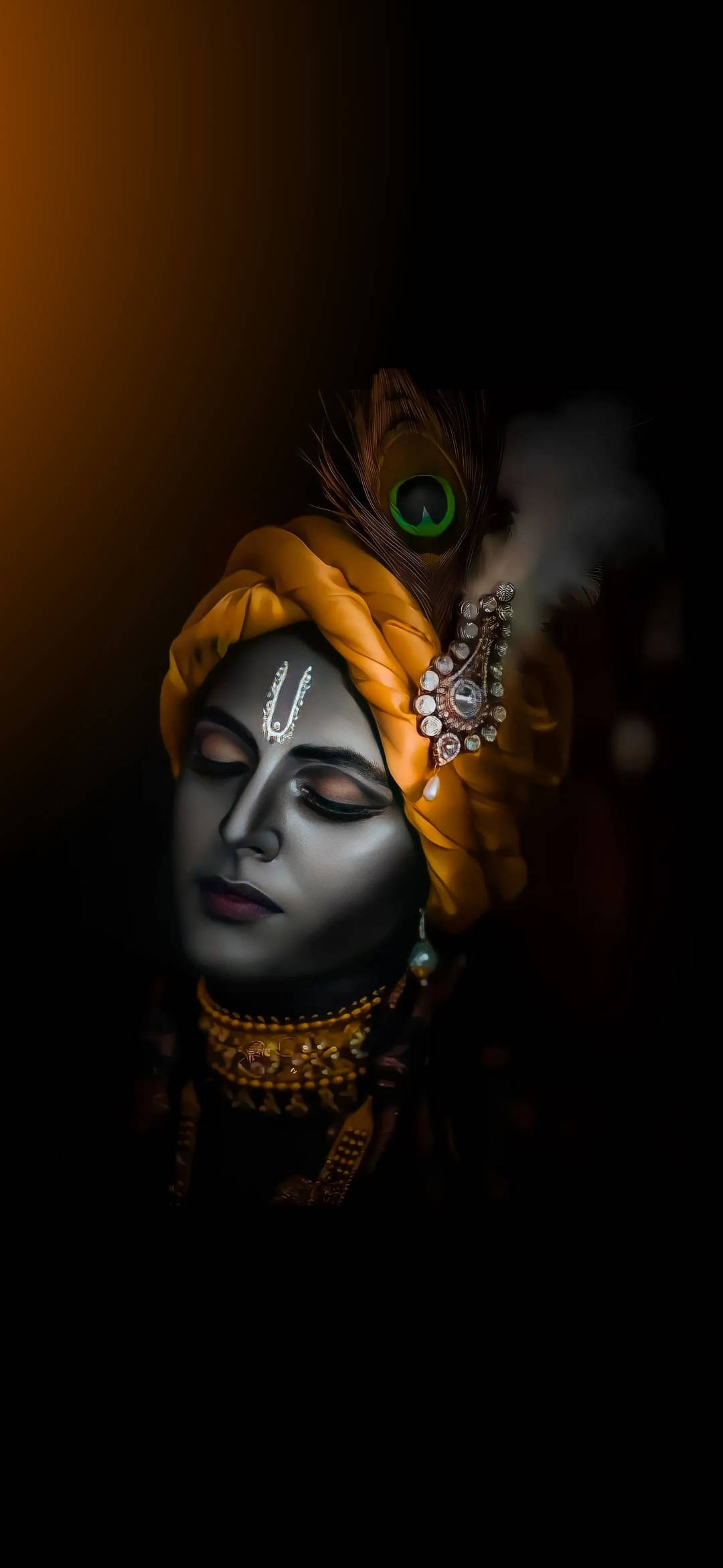 krishna iPhone 桌布 壁紙 — 一位皮膚黝黑、閉著眼睛、戴著金色頭巾、飾有孔雀羽毛和珠寶的神祇的寧靜肖像，背景為深色。