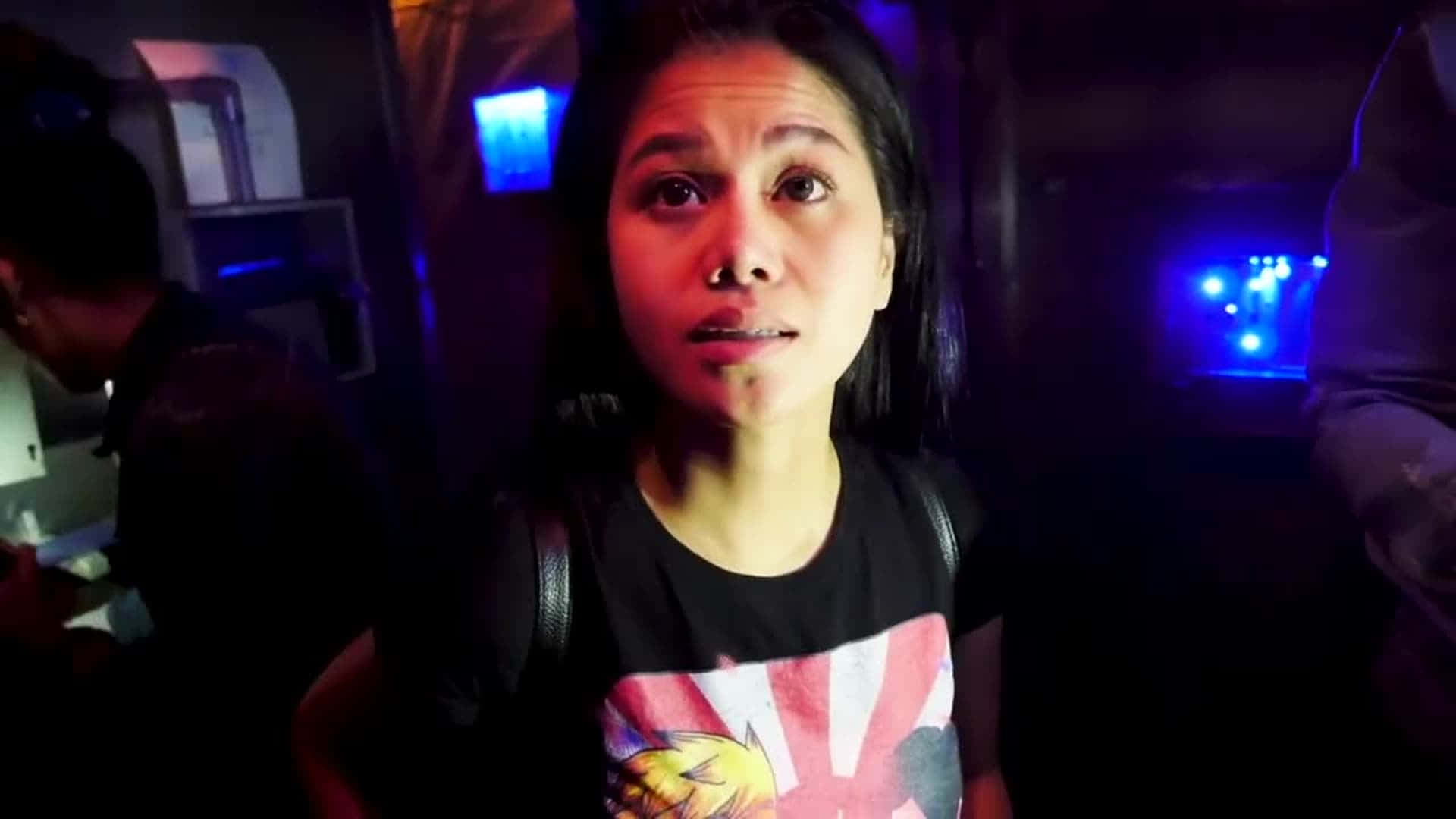 Woman 桌布 壁紙 — 一位眼睛睜大的女性在昏暗的房間中，沐浴在藍色霓虹燈光下，直視鏡頭。