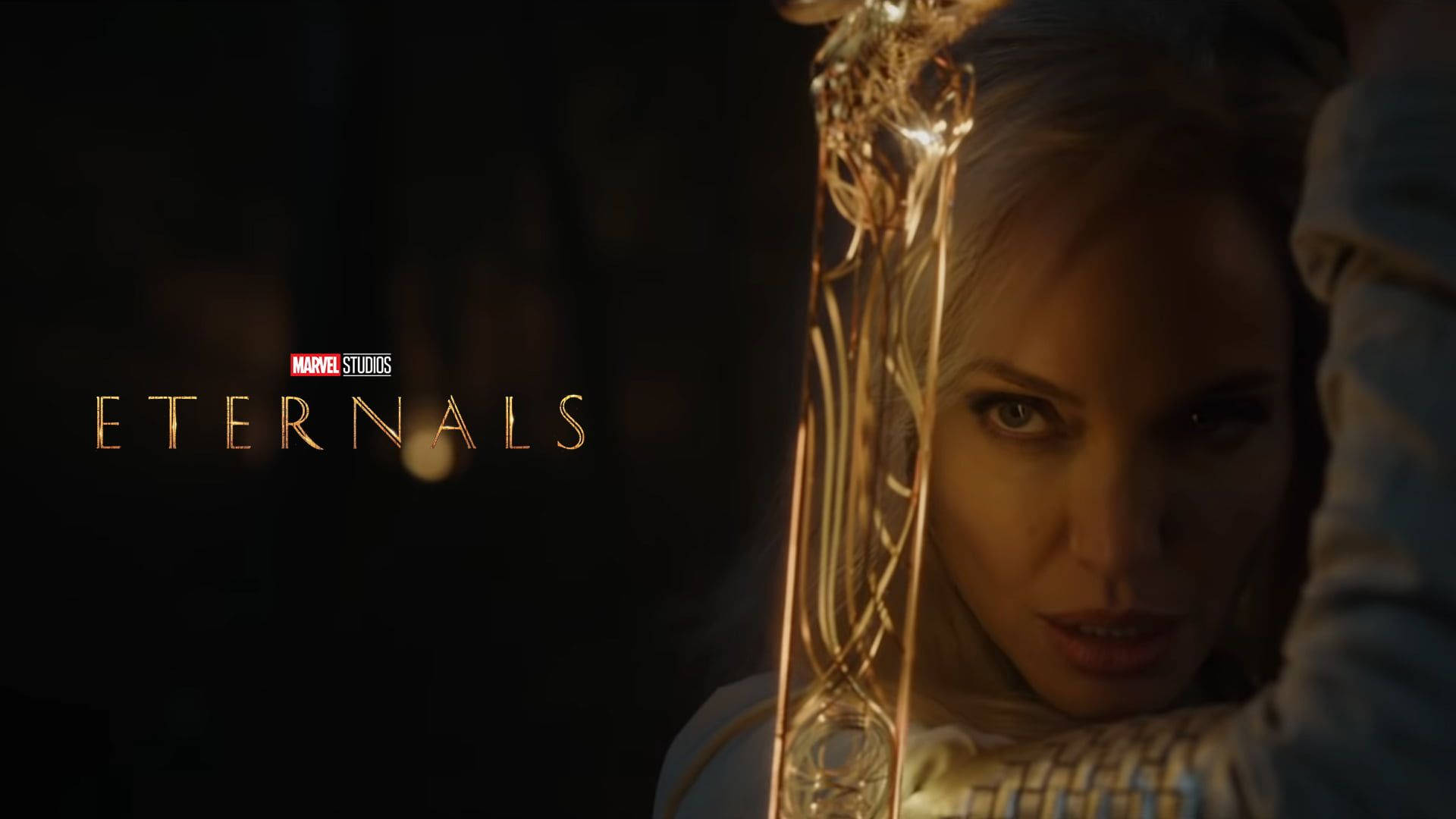 Eternals 桌布 壁紙 — 一位眼神銳利的女性在黑暗背景中握著一把發光的金色劍，並帶有「Eternals」標題。
