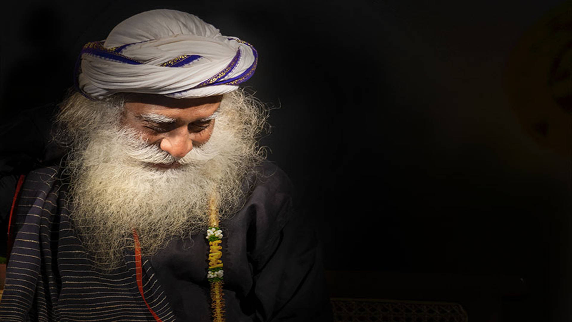 Indian 桌布 壁紙 — 一位睿智的長者，留著長長的白鬍子，戴著頭巾，在黑暗的背景中靜靜地沉思，向下凝視。