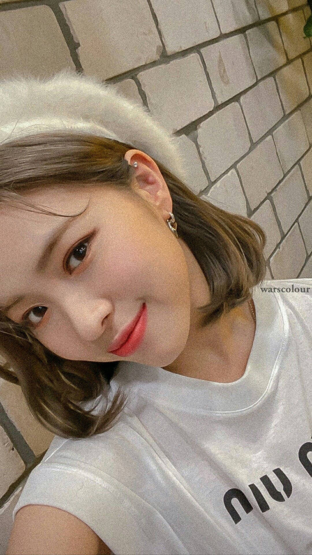 ITZY 桌布 壁紙 — 一位短棕髮、戴白色毛絨頭帶的年輕女性，在淺色磚牆背景下溫柔微笑。