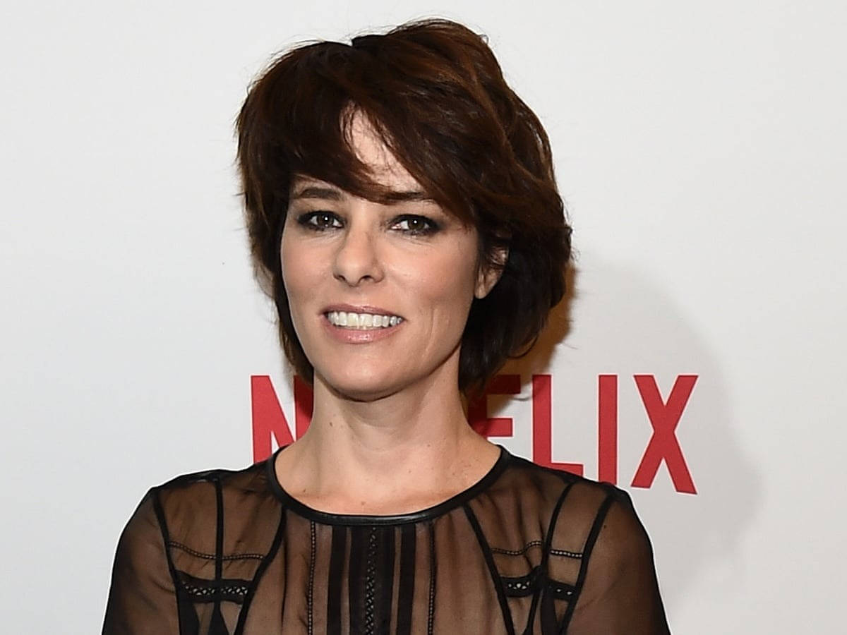 Netflix 桌布 壁紙 — 一位短棕髮女性穿著黑色透視上衣，在白色背景前帶有紅色Netflix標誌，對著鏡頭微笑。