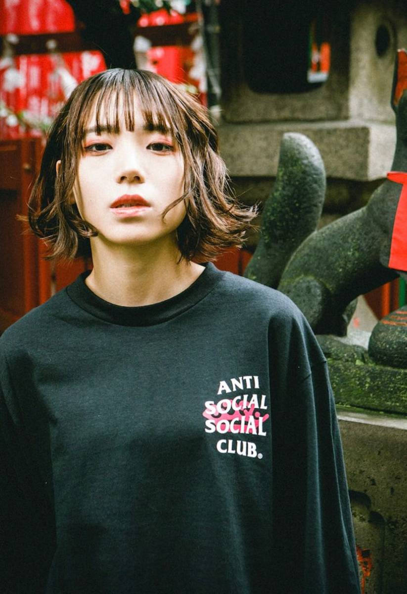 club 桌布 壁紙 — 一位短棕髮年輕女性穿著印有 'ANTI SOCIAL SOCIAL CLUB' 文字的黑色運動衫，站在一個有紅色燈籠的石造神社前。