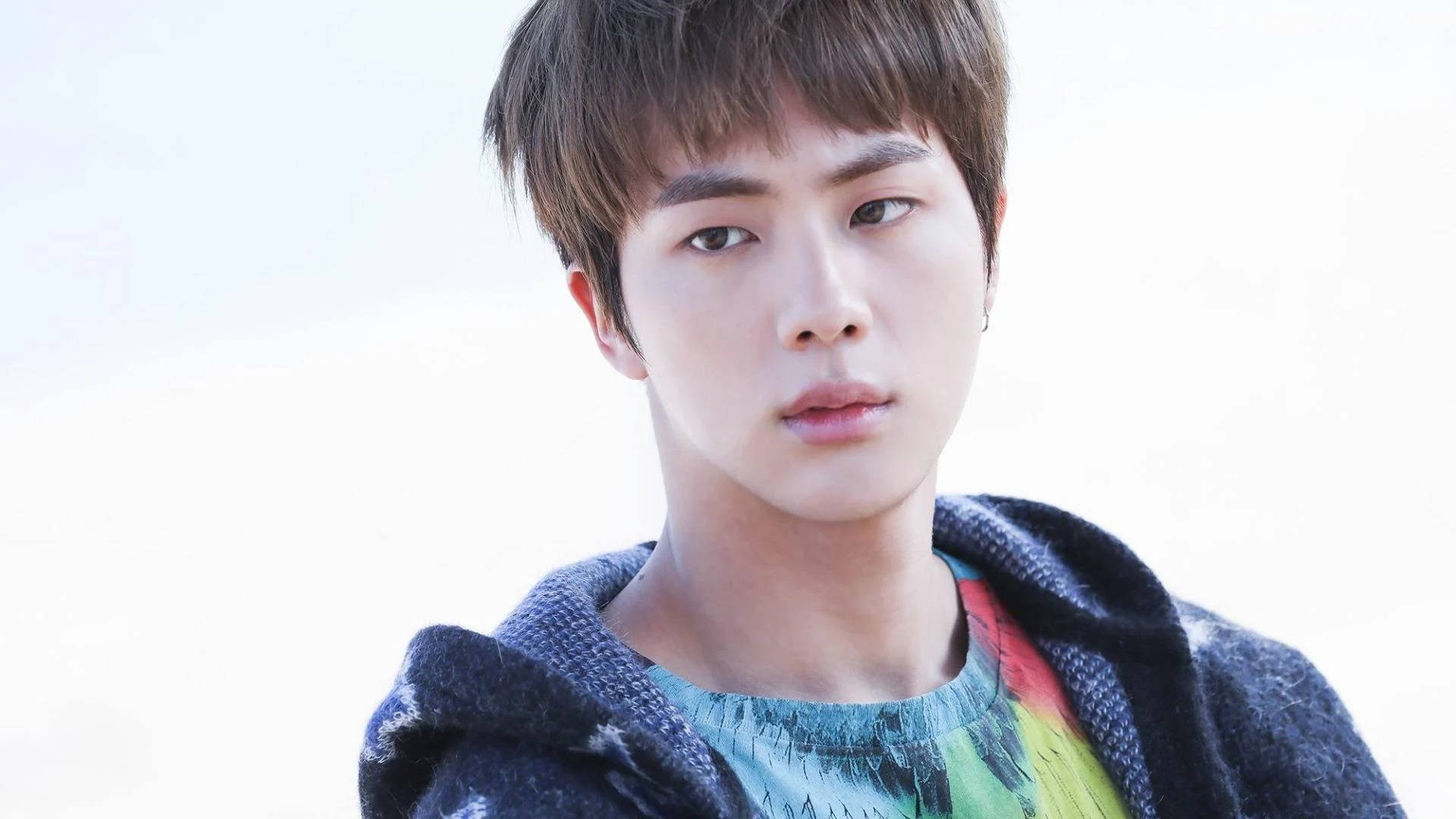 Jin 桌布 壁紙 — 一位短棕髮的年輕男子在明亮的白色背景前，穿著深色連帽衫，內搭彩色襯衫。